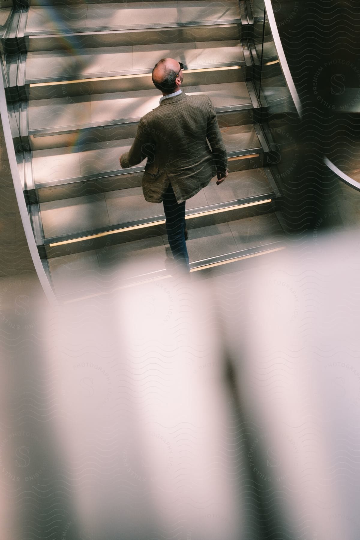 A bald man in sunglasses walks up a modern staircase.