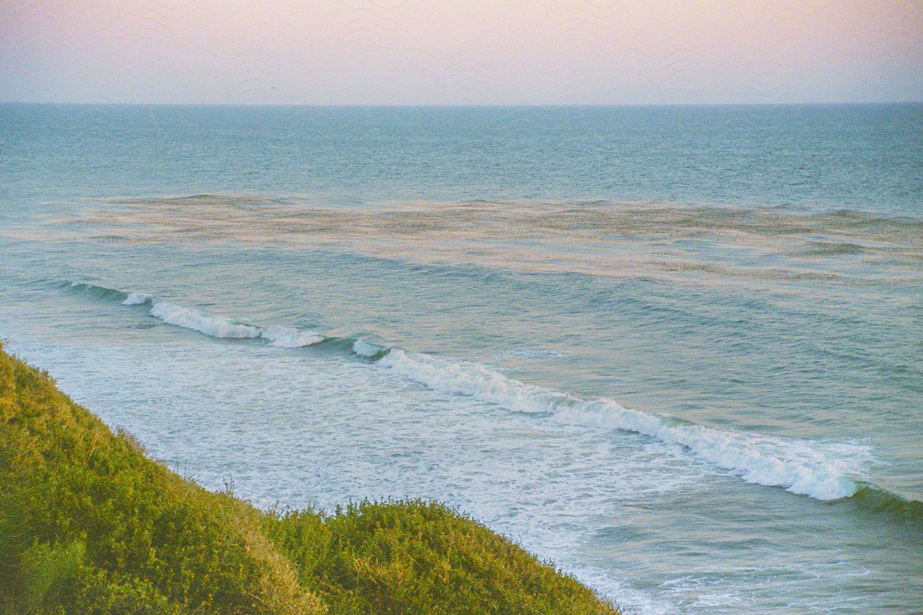 the waves from the ocean hit the coastline covered in green grass