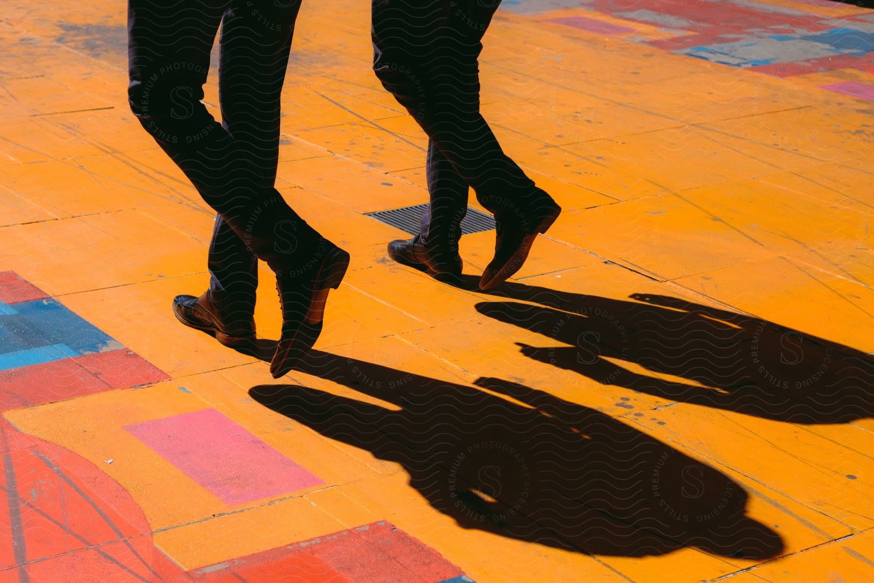 The legs of two men walking down a brightly colored tiled walkway.