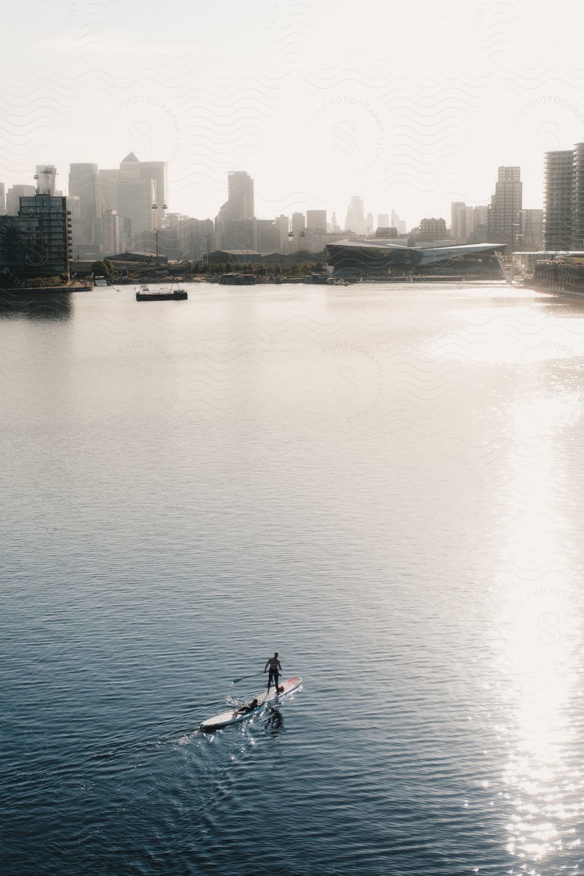 Two people on longboards swimming or paddling towards a coastal city.