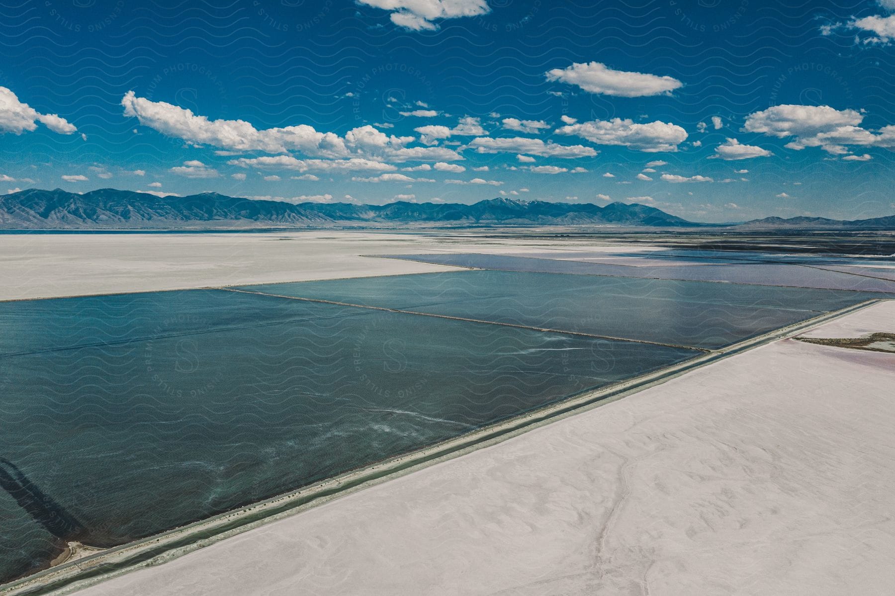 Canal near the salt flats with mountains in the distance with cumulus clouds in a blue sky