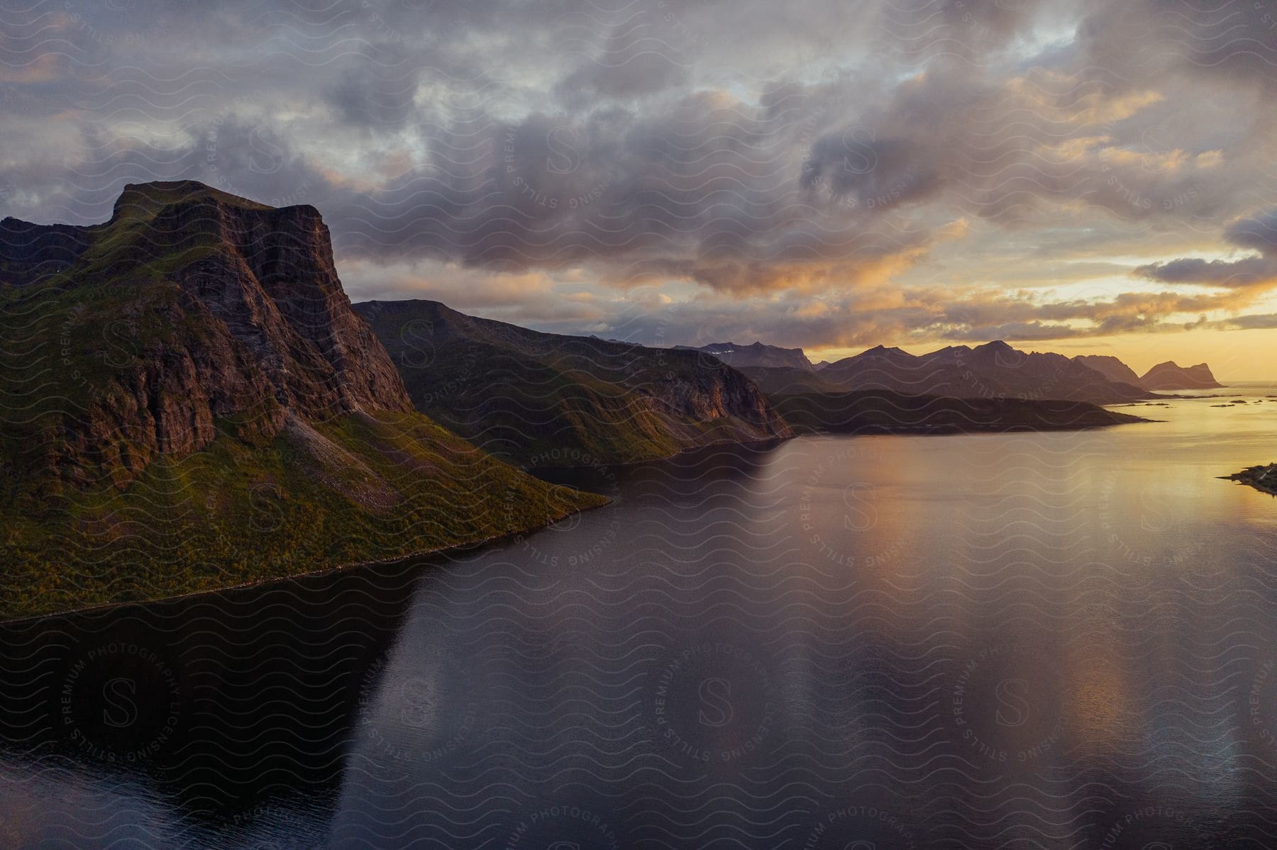 a large body of water surrounded by mountains with green valleys and clouds at sunset