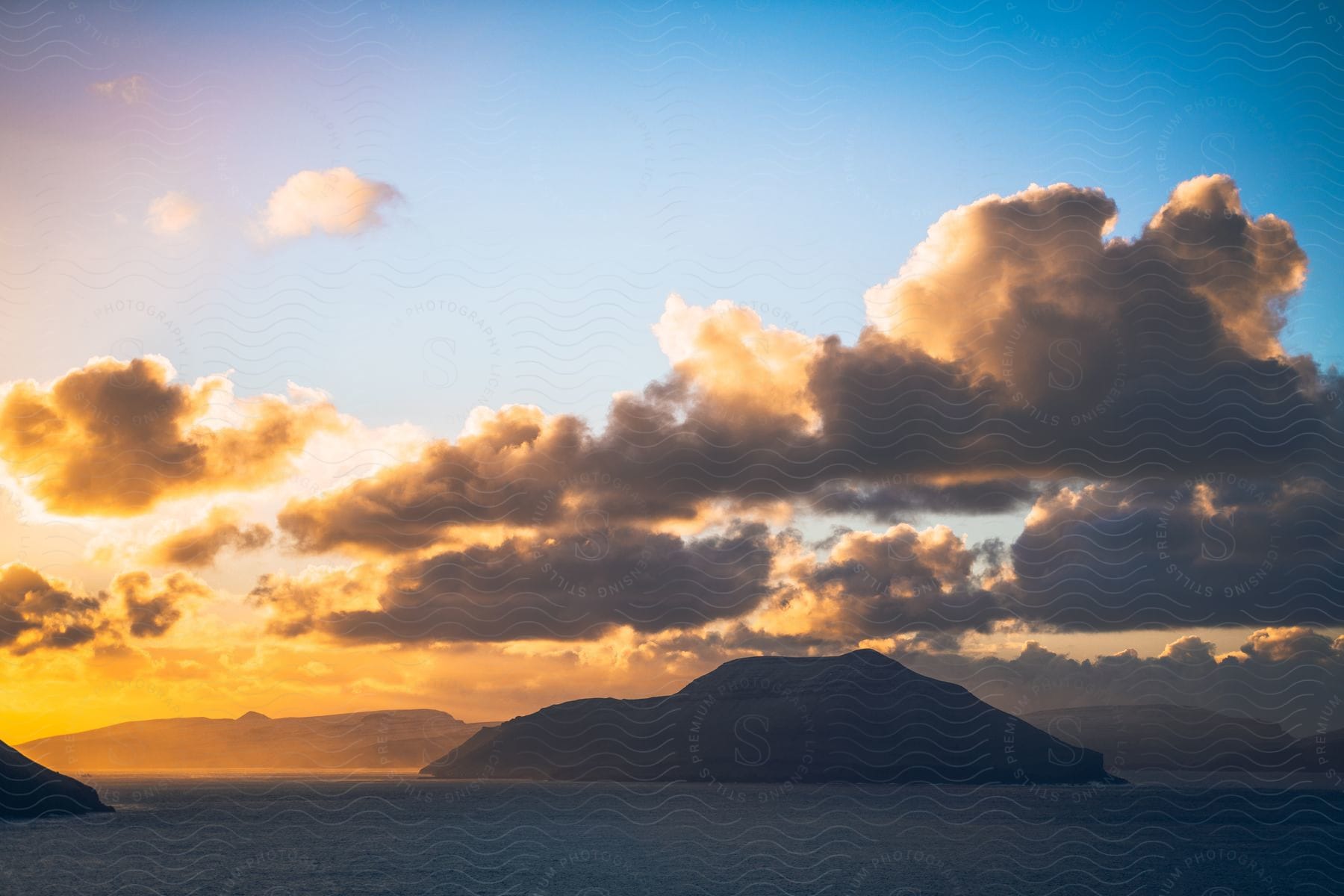 Sun shining through clouds turns horizon golden as it back lights island.