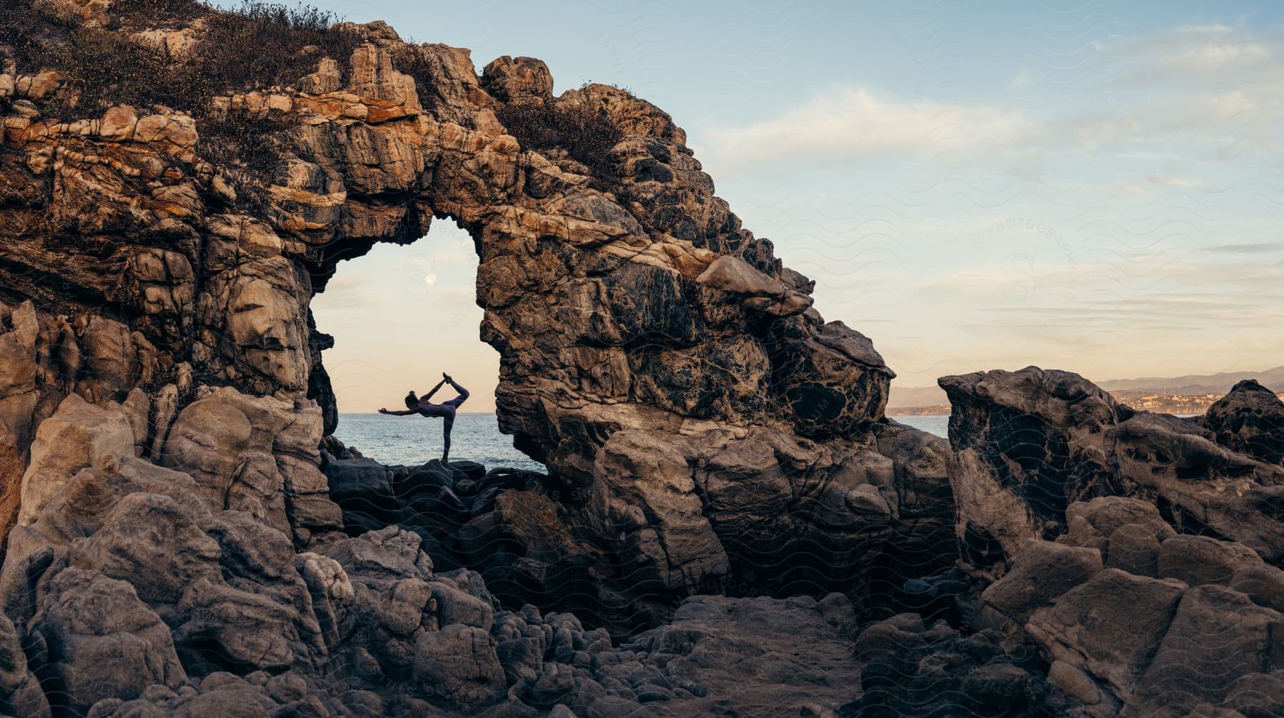 a woman stretches while doing yoga on rocks along the coast