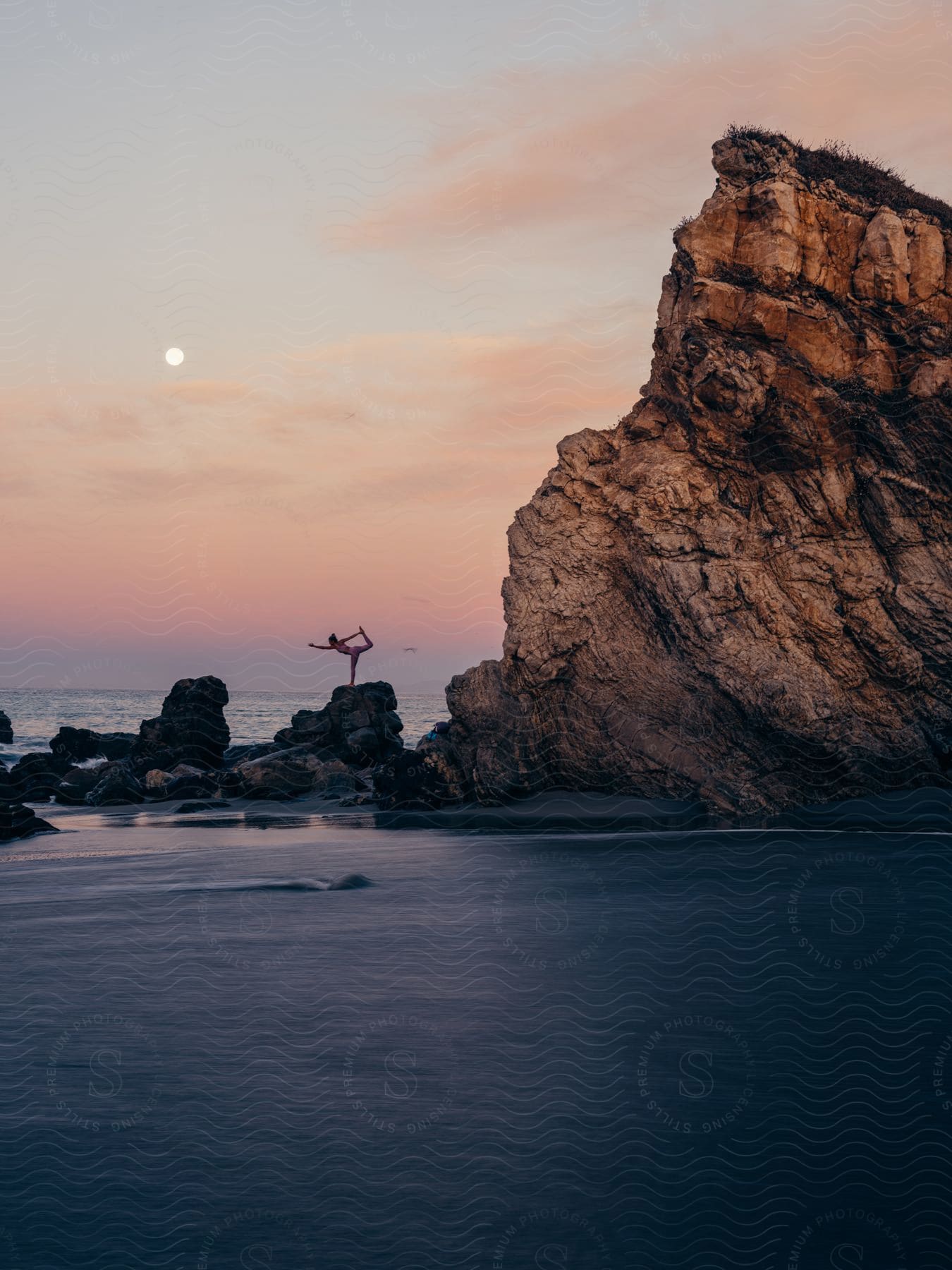 A woman is doing yoga on the beach at sunset.