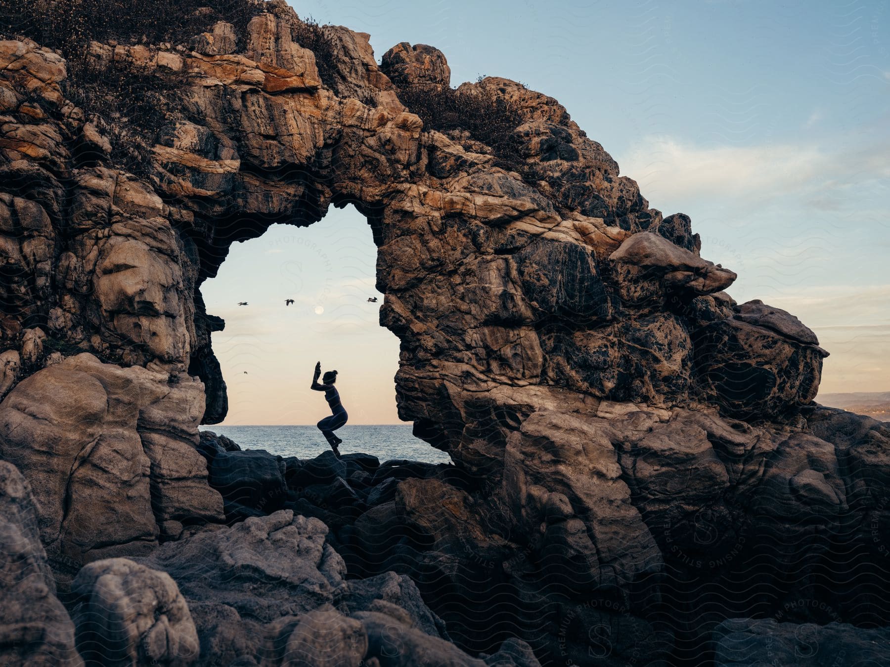 a woman holds a yoga pose on rocks along the coast