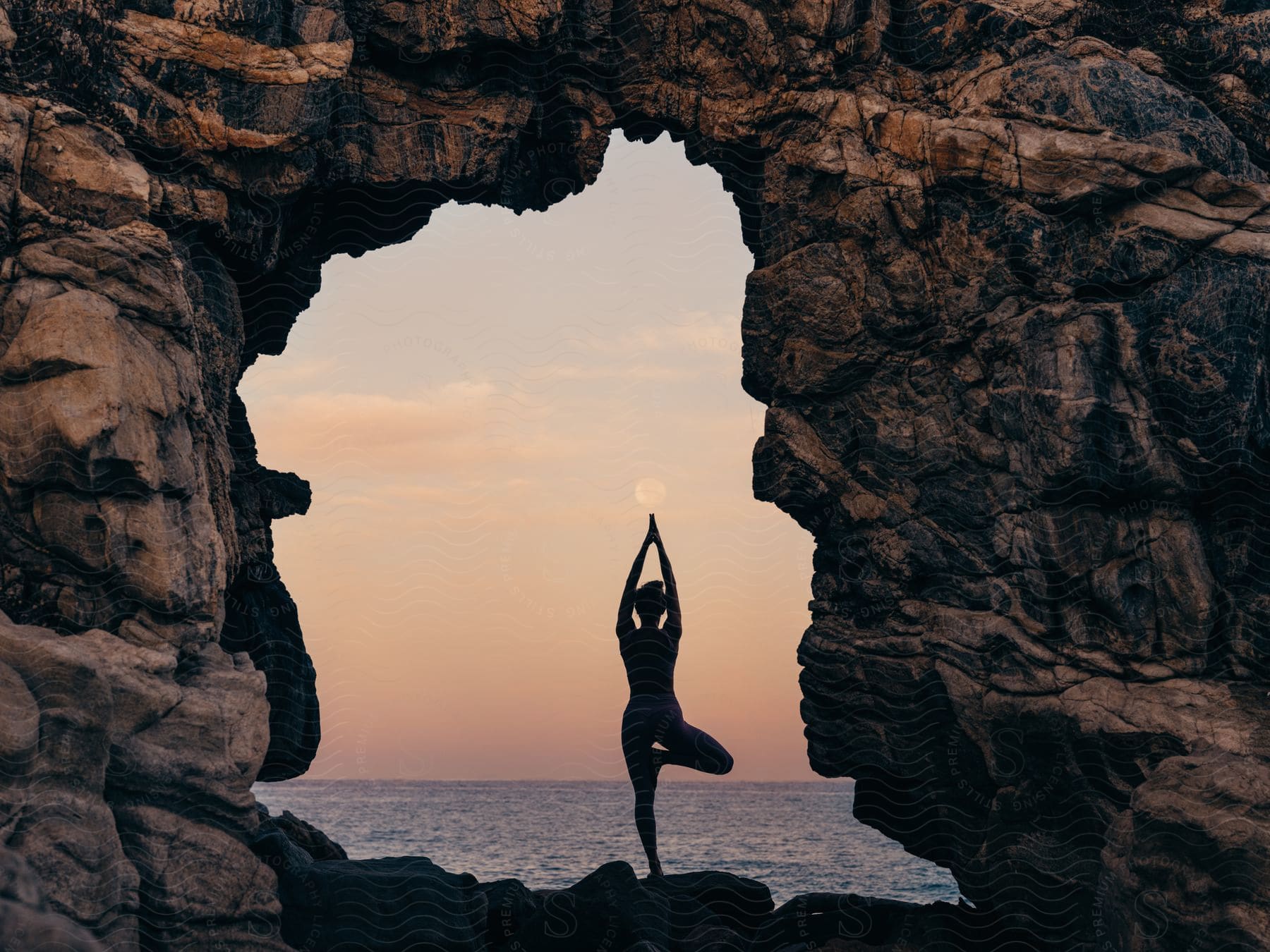 a woman doing yoga on a rocky beach near the ocean at sunset