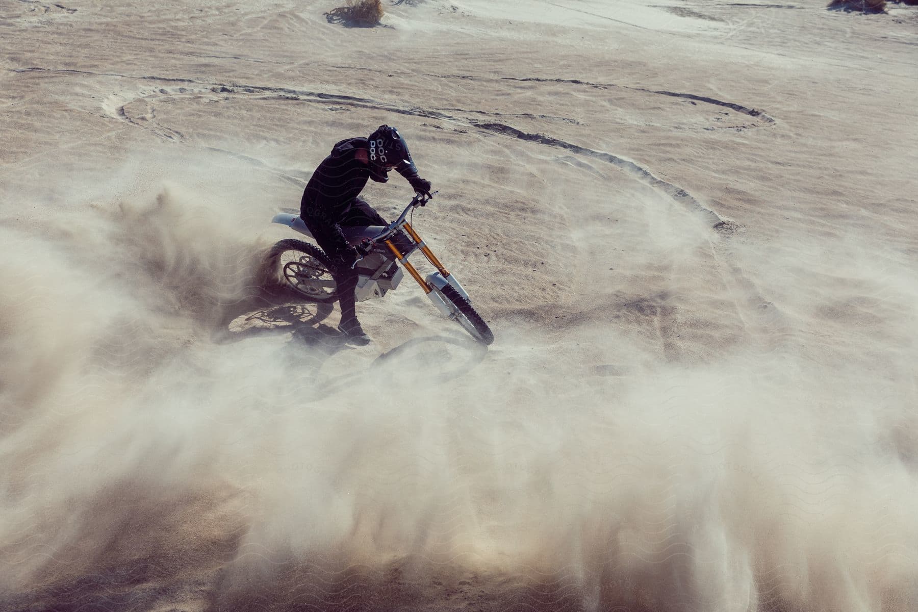 A person on top of a motorcycle that has just made maneuvers and kicked up a lot of sand.