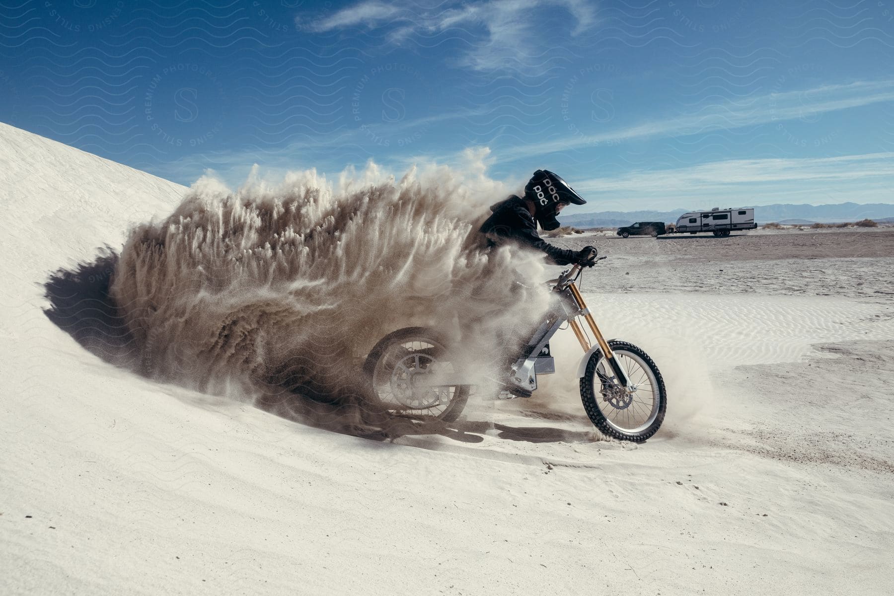 An off-road motorcyclist kicks up desert sand on a dune.