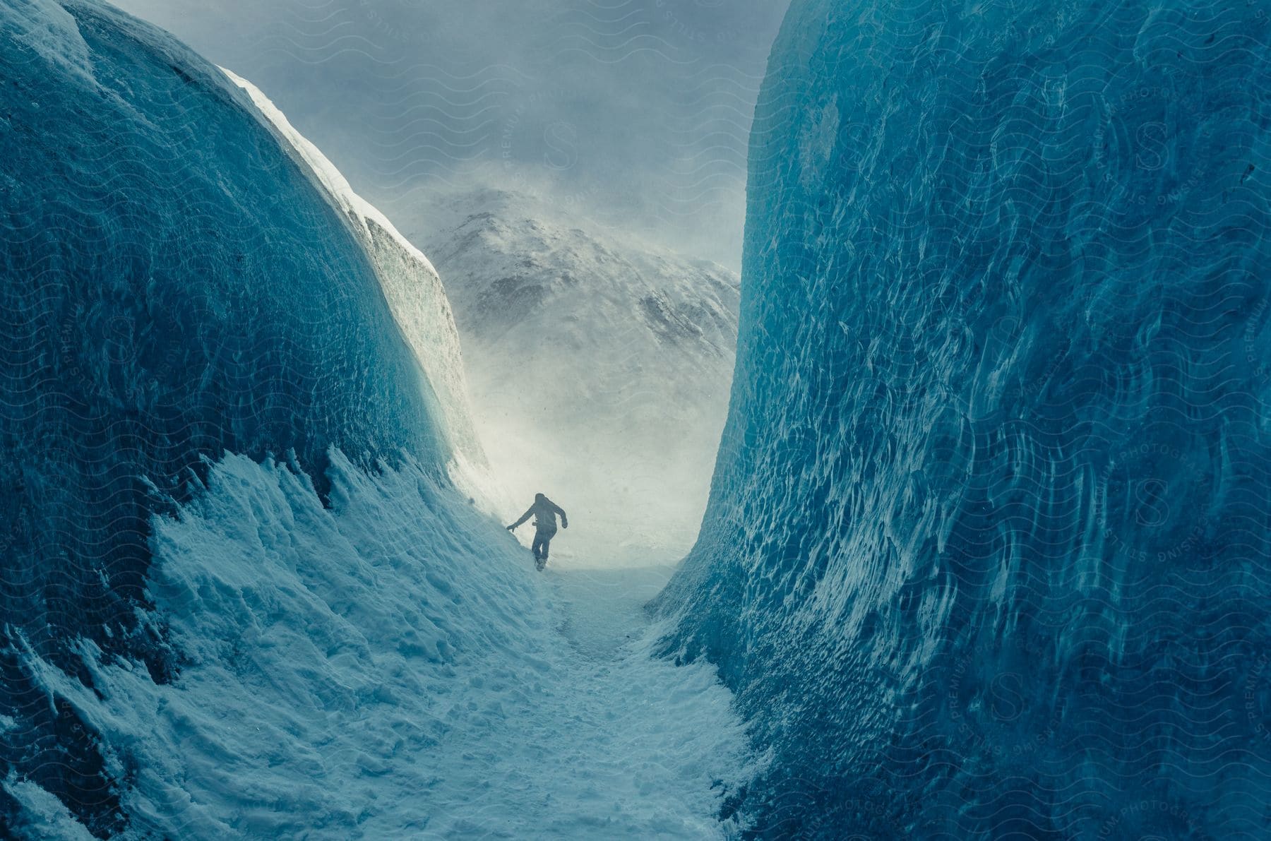 A person is walking on the snow beetween two mountains.