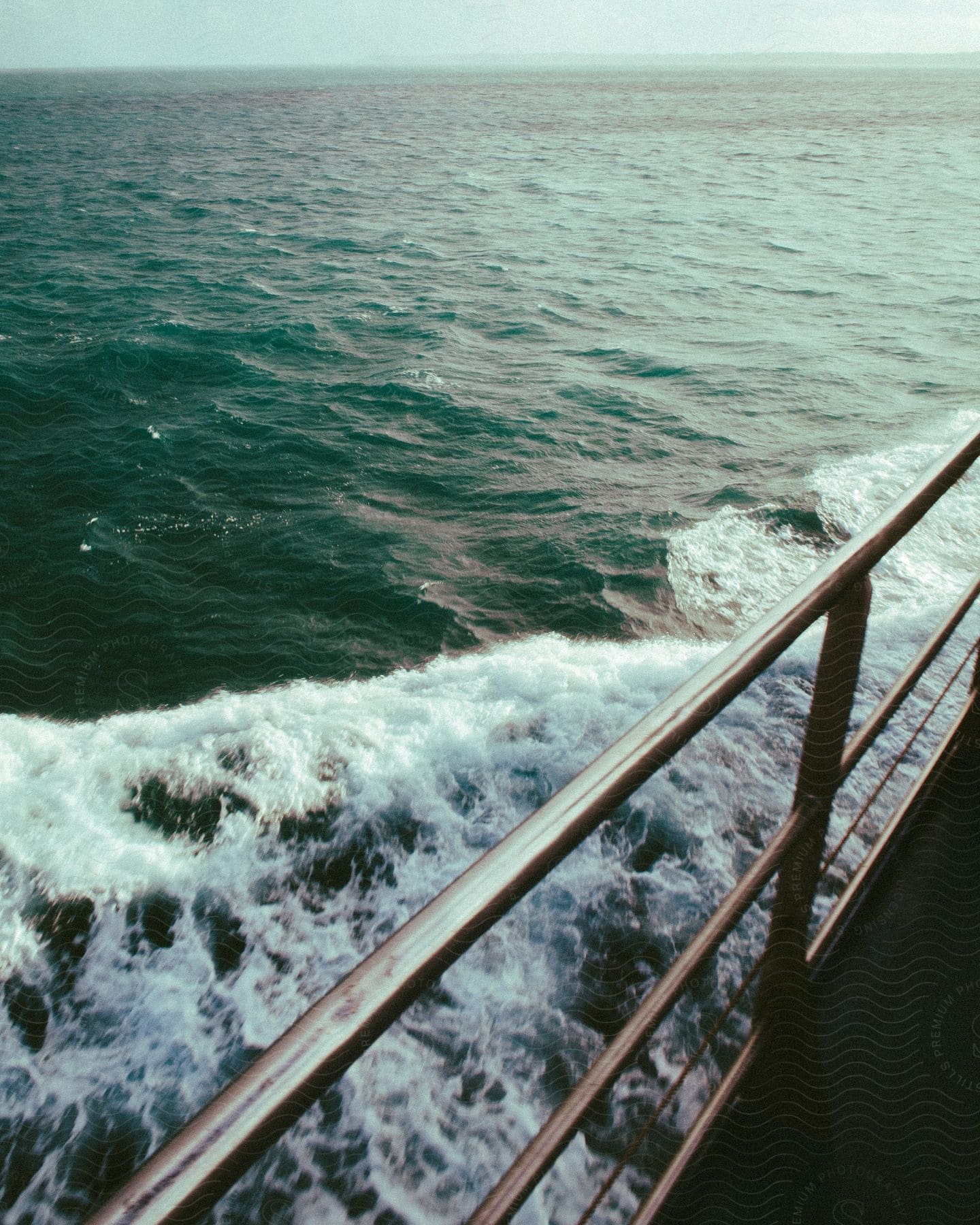 A view of the ocean from aboard a ship with a coastline barely visible in the distant haze in the day.