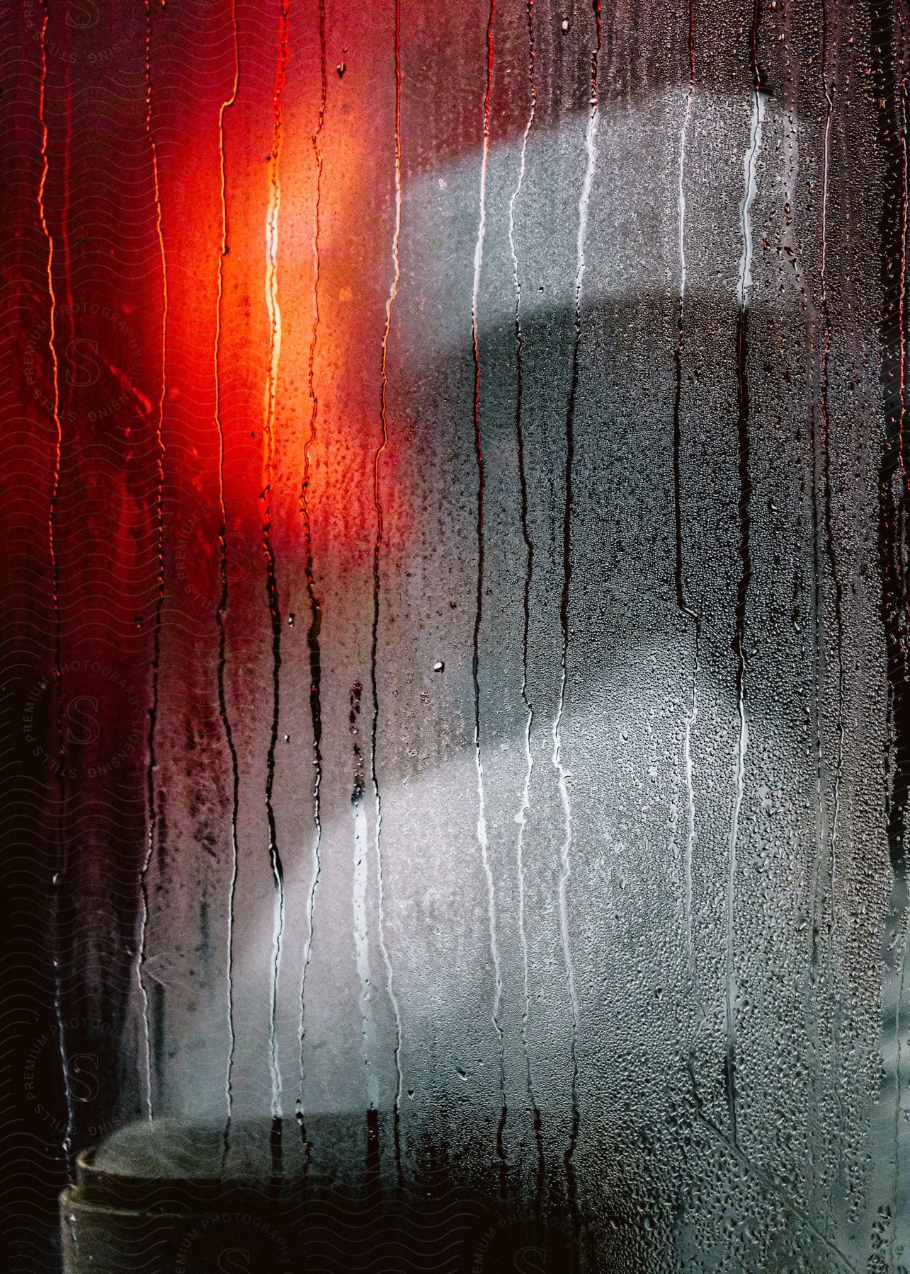 Water streaks down a moisture covered window as a woman stands inside