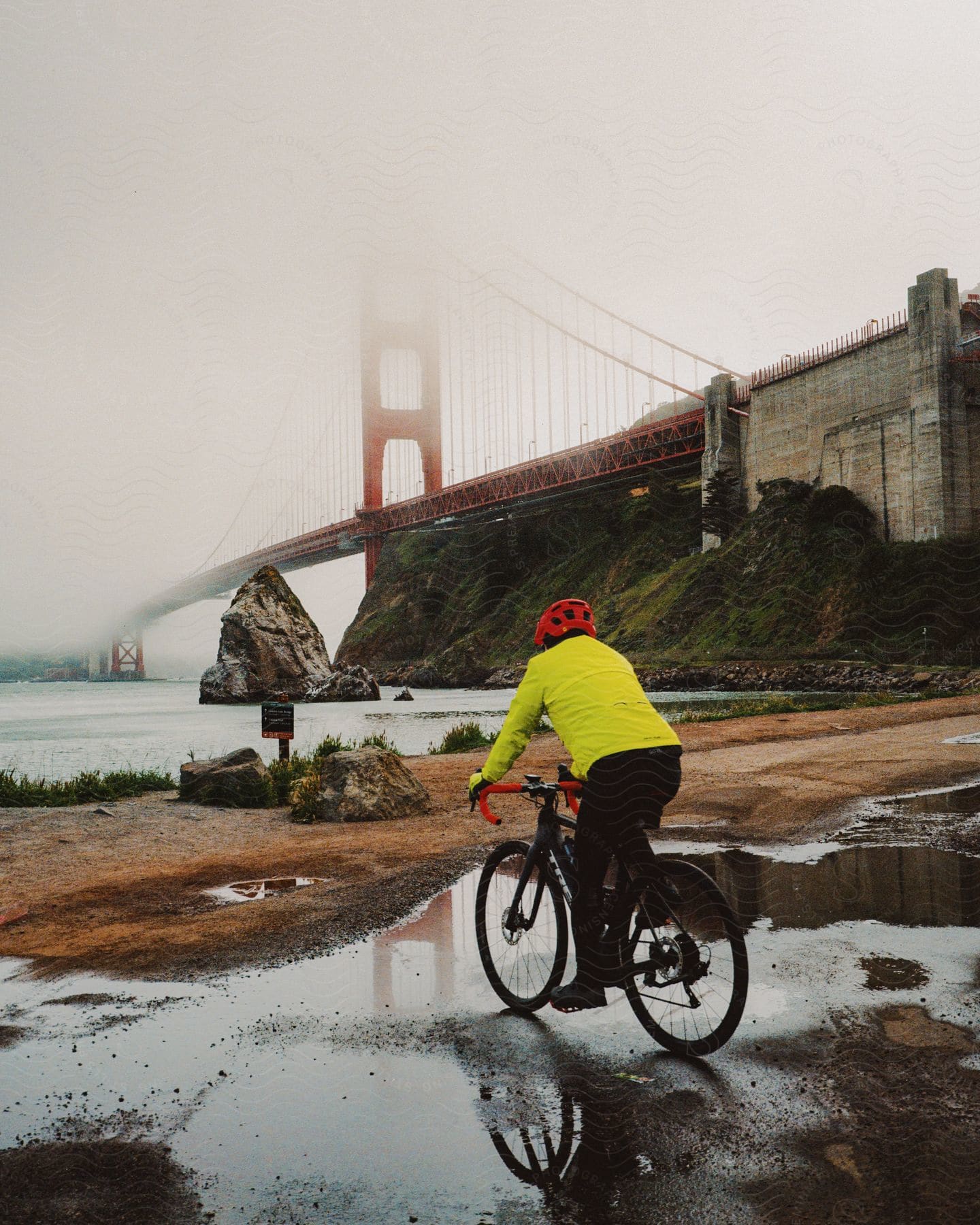 A man in a bicycle with a yellow jacket starring at the coast of the sea and the Golden Gate bridge.