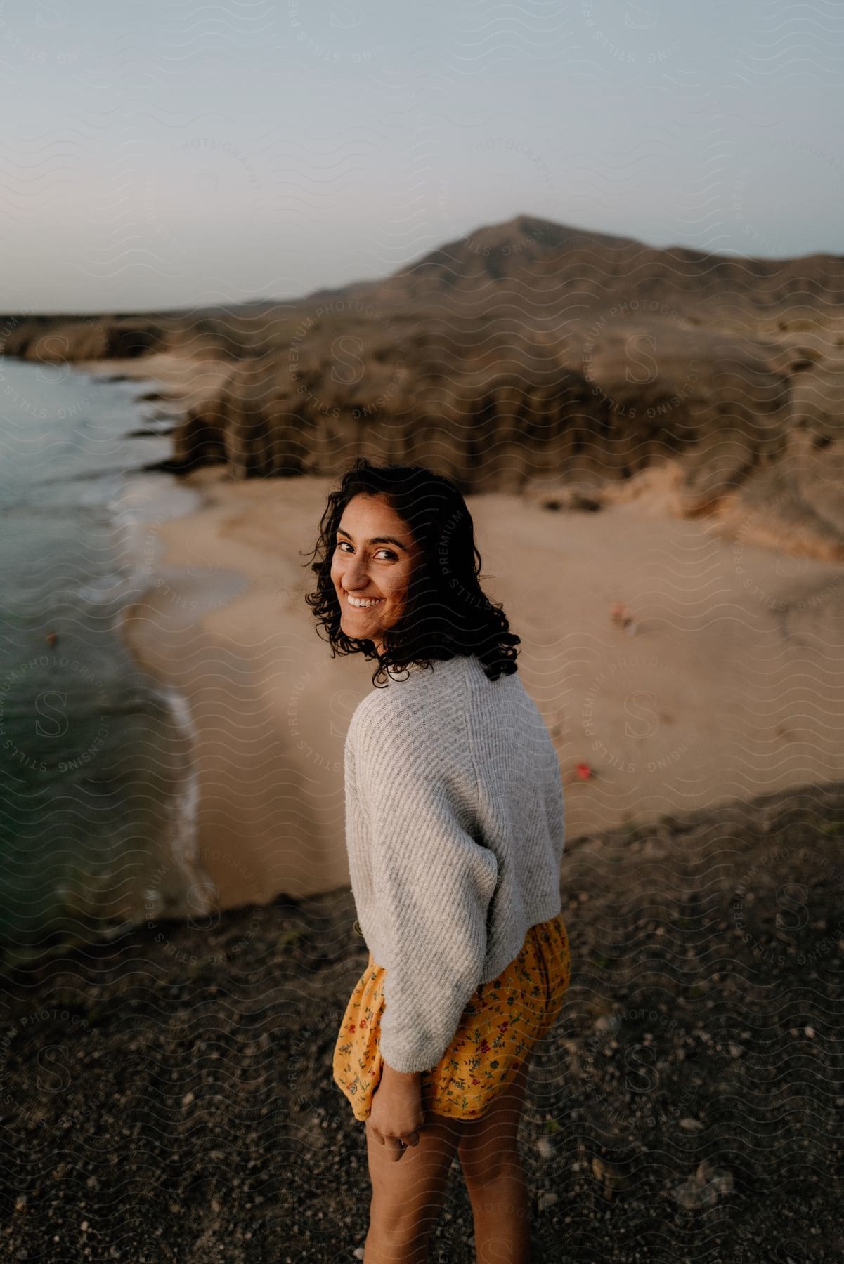 Woman smiling on a beach with a mountain on the horizon.