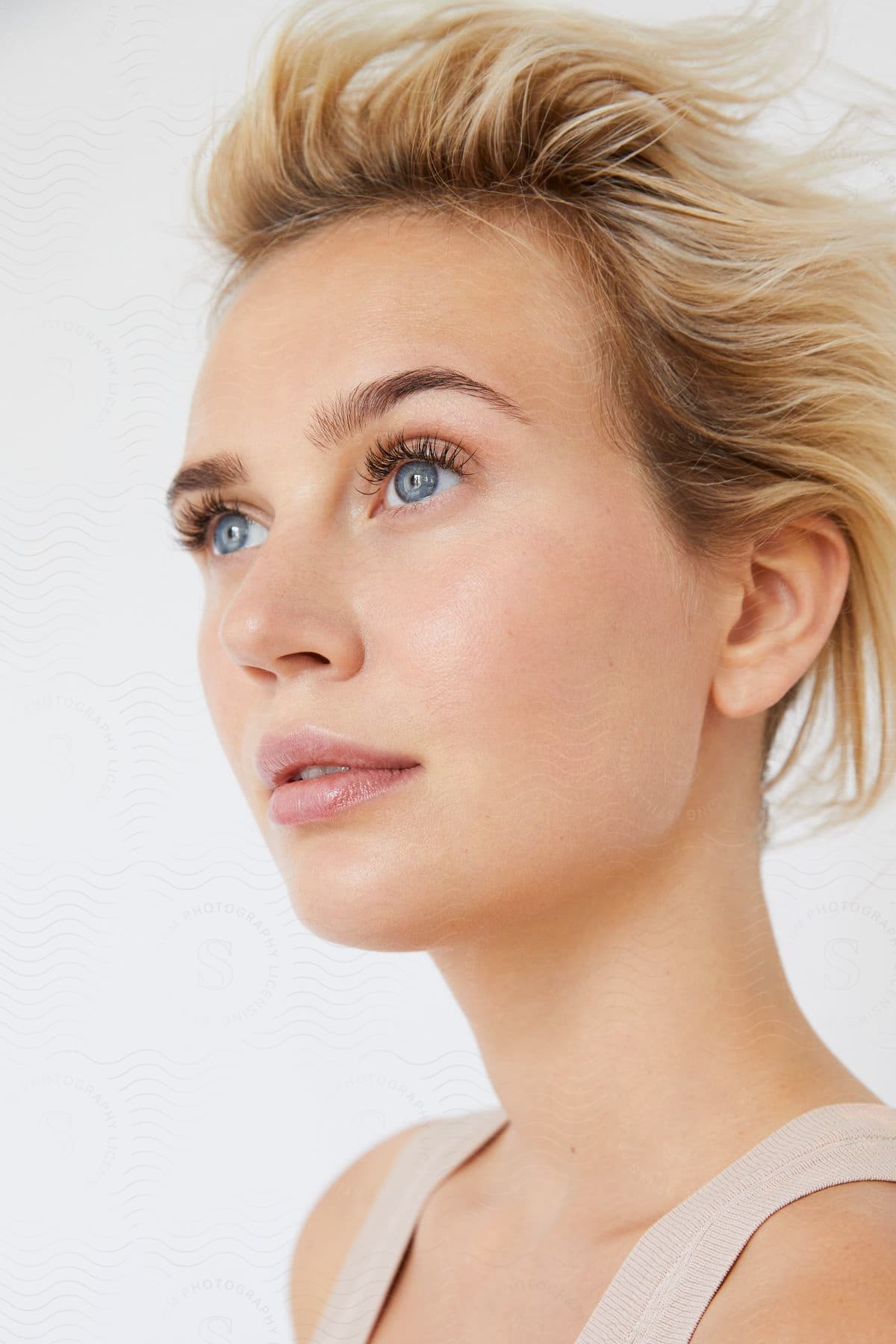 A woman with short blonde hair and blue eyes is gazing outward