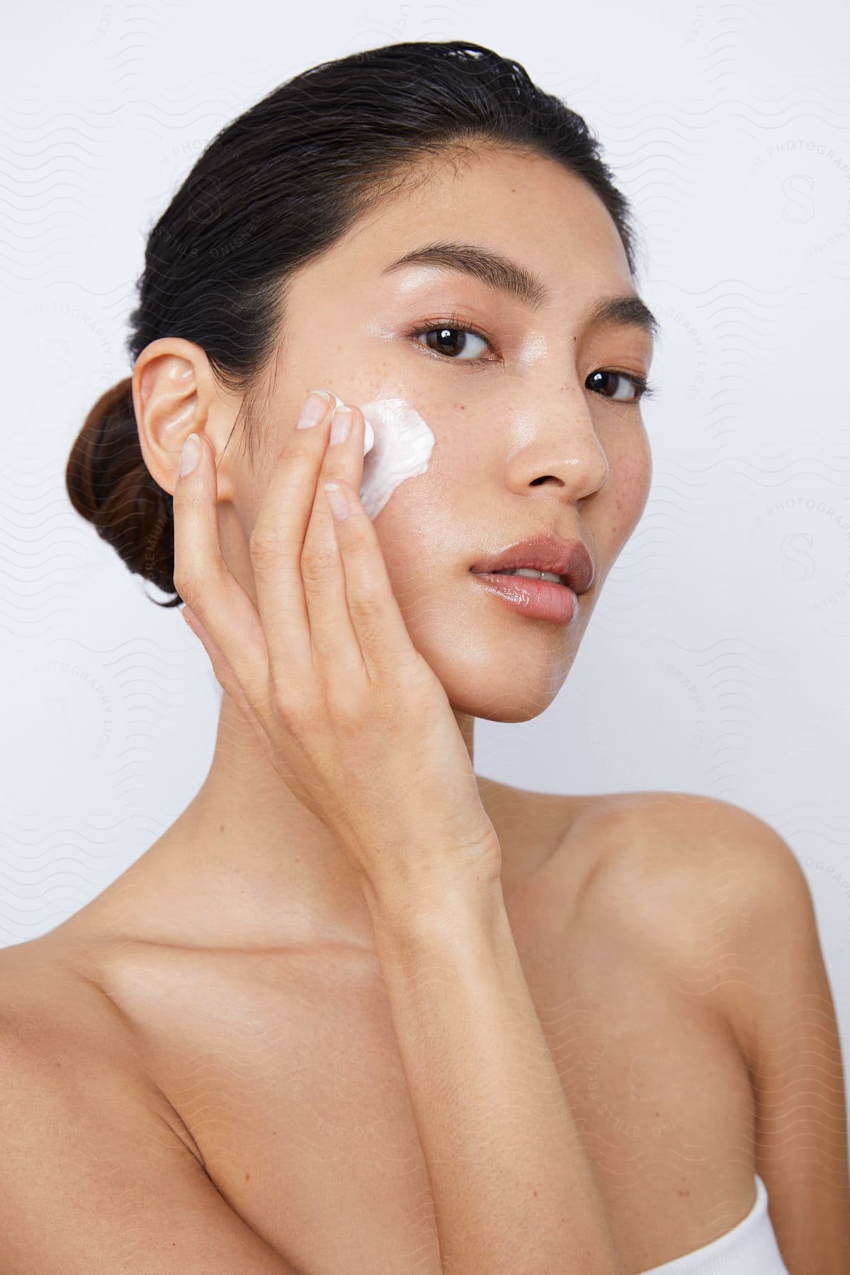 A woman is rubbing white cream on her face with her fingers