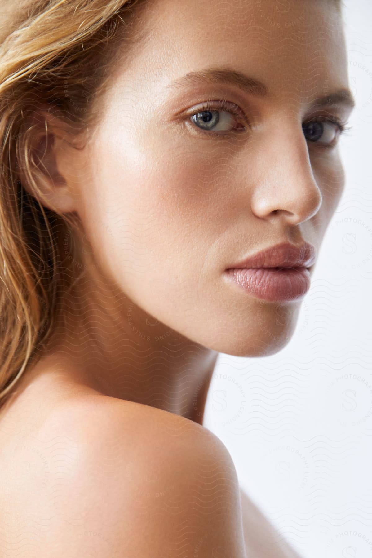 A woman with blue eyes and beautiful lips looking over her bare shoulder