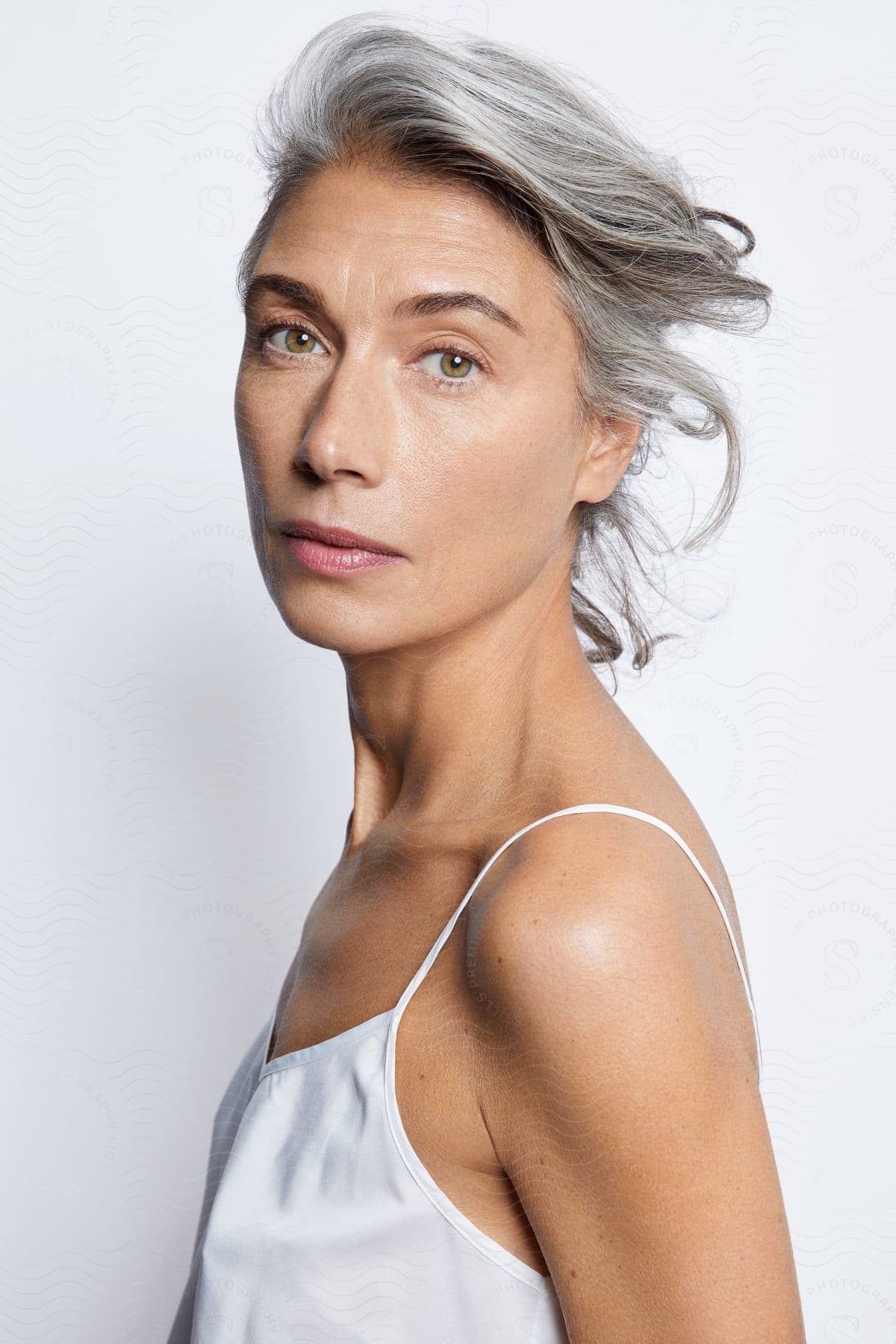 A middle-aged woman poses for the camera while wearing a white camisole.