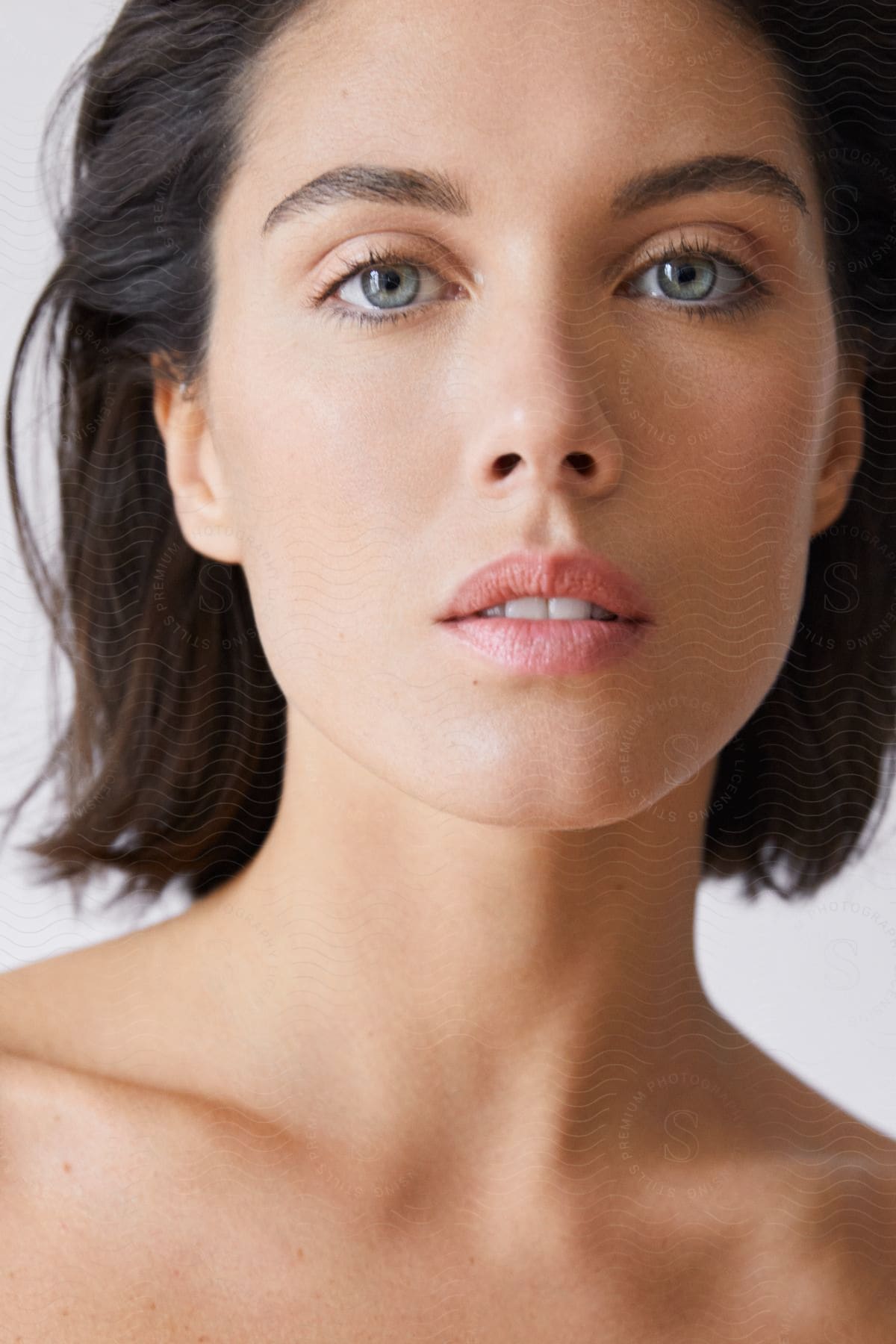 A woman with dark brown hair and blue eyes is looking ahead with her mouth partially open