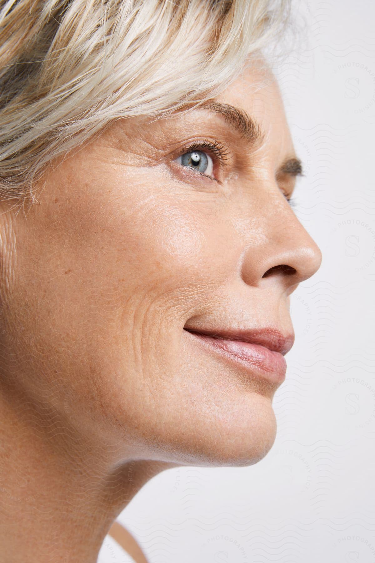 Blonde woman with smile wrinkles around her eyes and mouth smiles slightly while looking to her right.