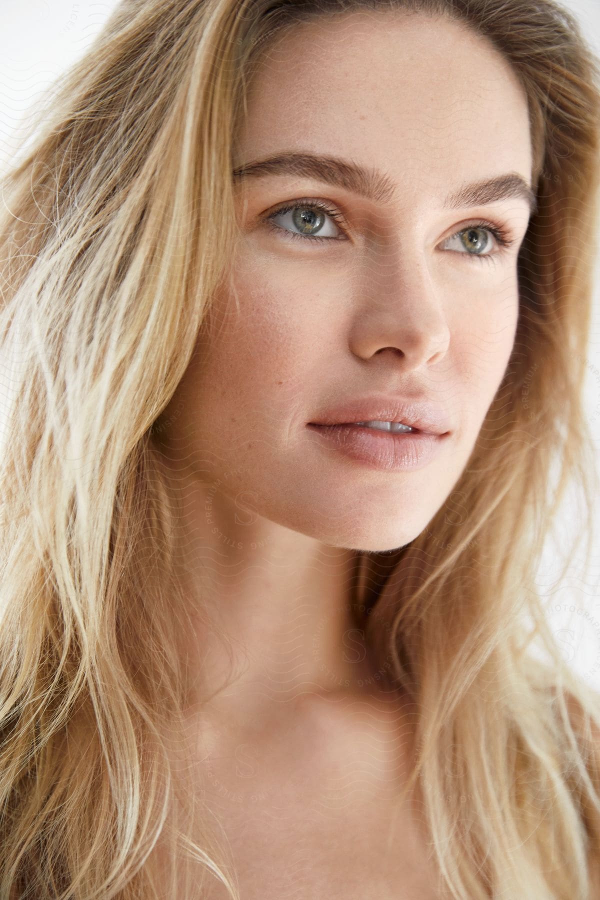 A woman with long blonde hair and blue eyes is looking ahead with her mouth partially open