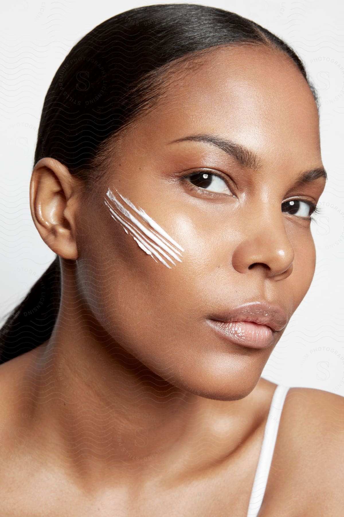 A woman with lines of white cream on her cheek is looking forward