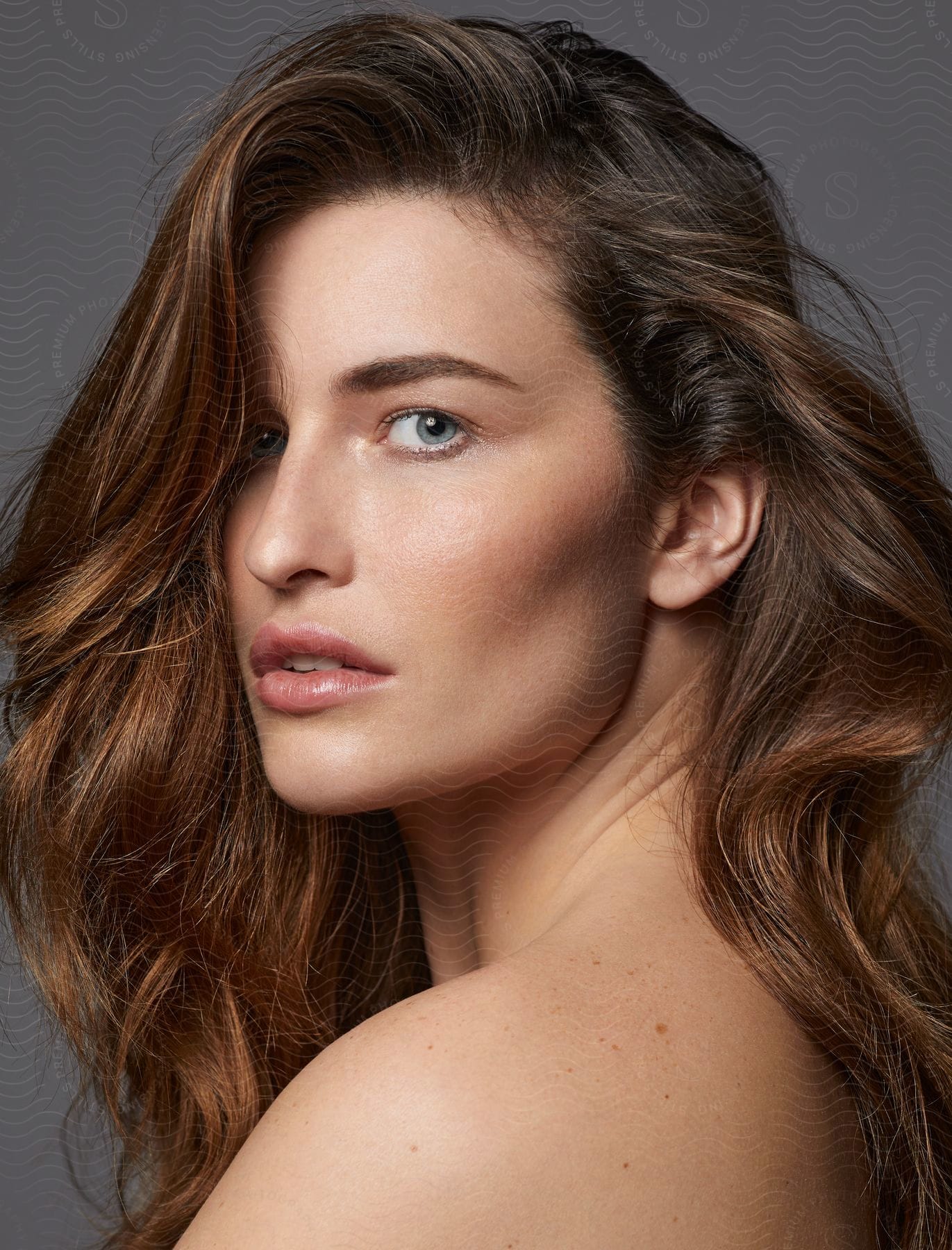 Woman with long brown hair turns her head to look over her shoulder.