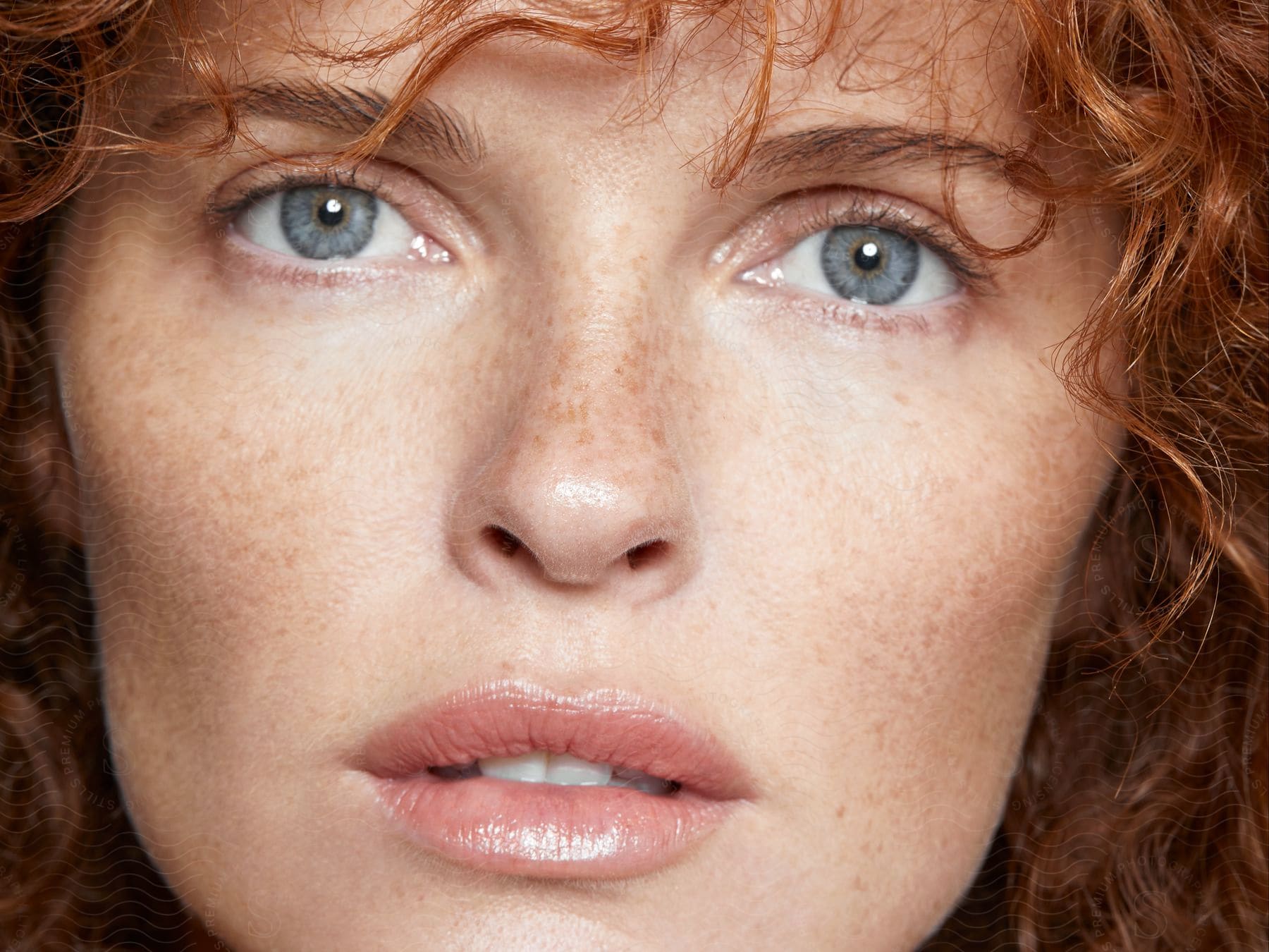 Face of a beautiful, freckled redhead woman with curly hair and blue eyes