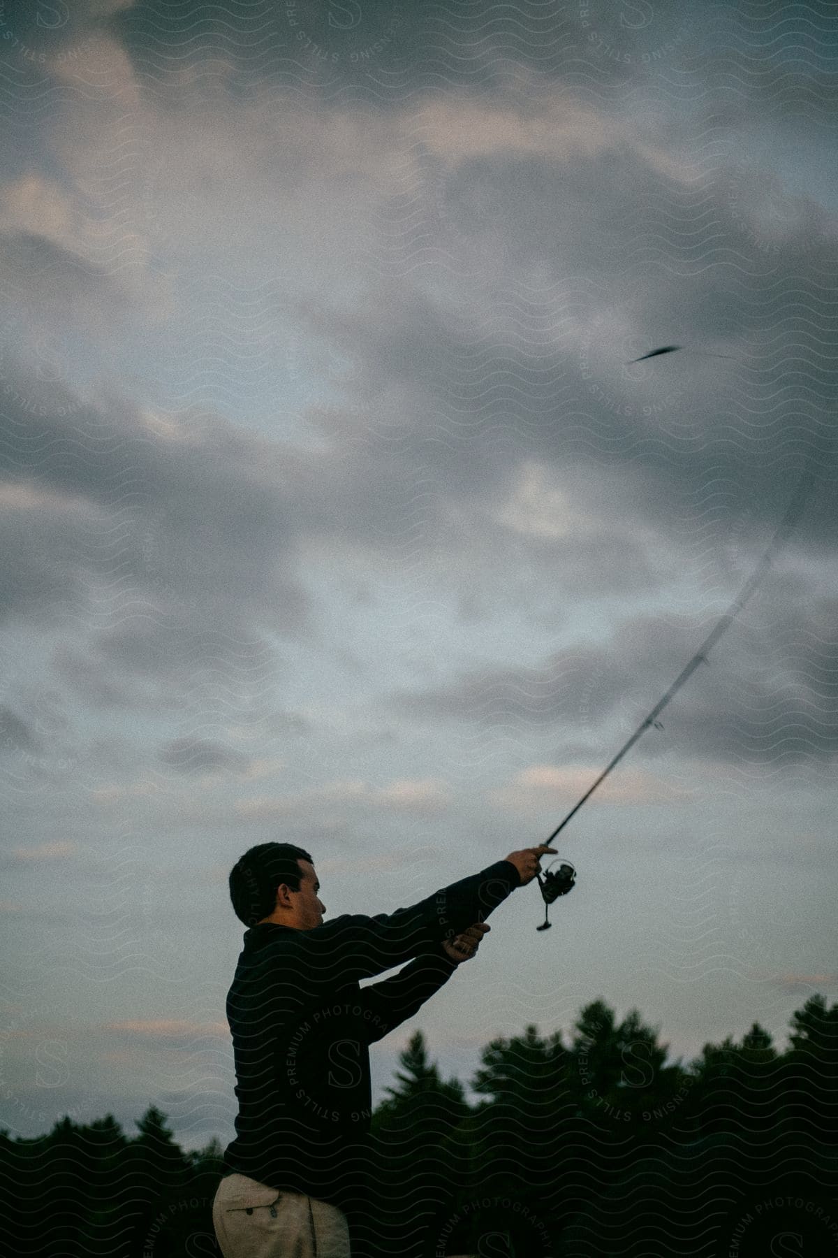 A fisherman is casting a lure with his fishing rod on a cloudy evening.