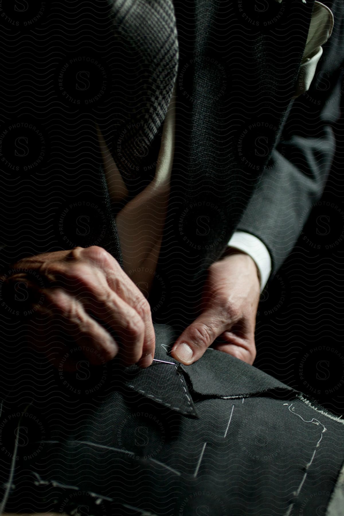 A man wearing a suit is sewing a dark material