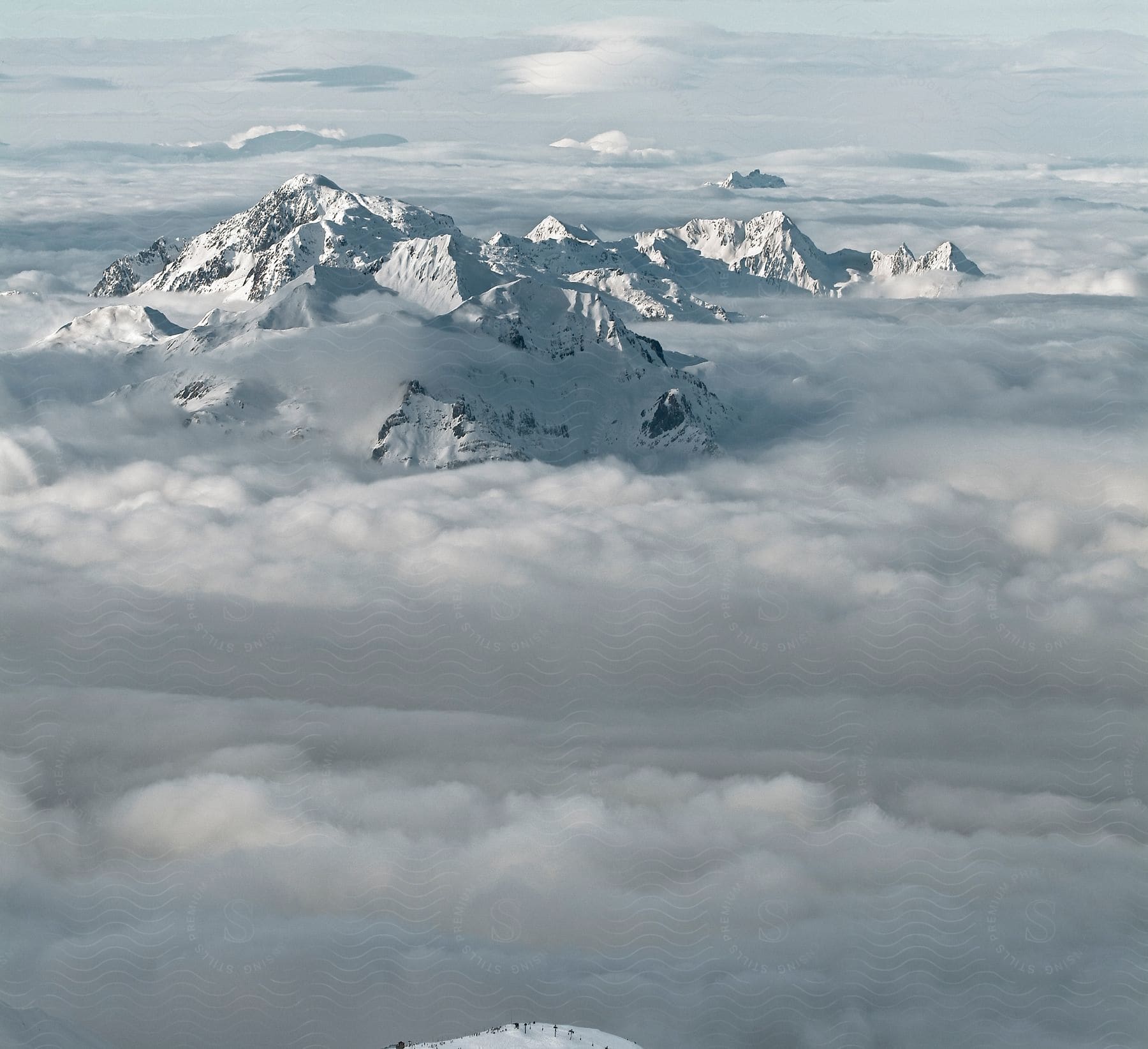 Stock photo of snow-capped mountain peaks emerge from the rolling clouds in the distance