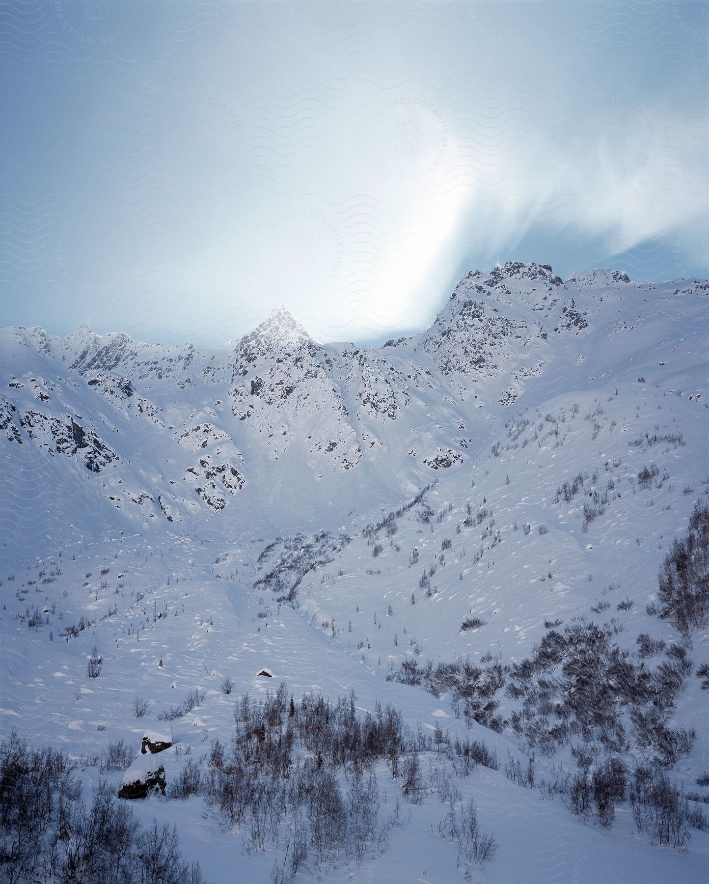 Snow Covers Rough Mountain Terrain As The Sun Shines Through The Clouds