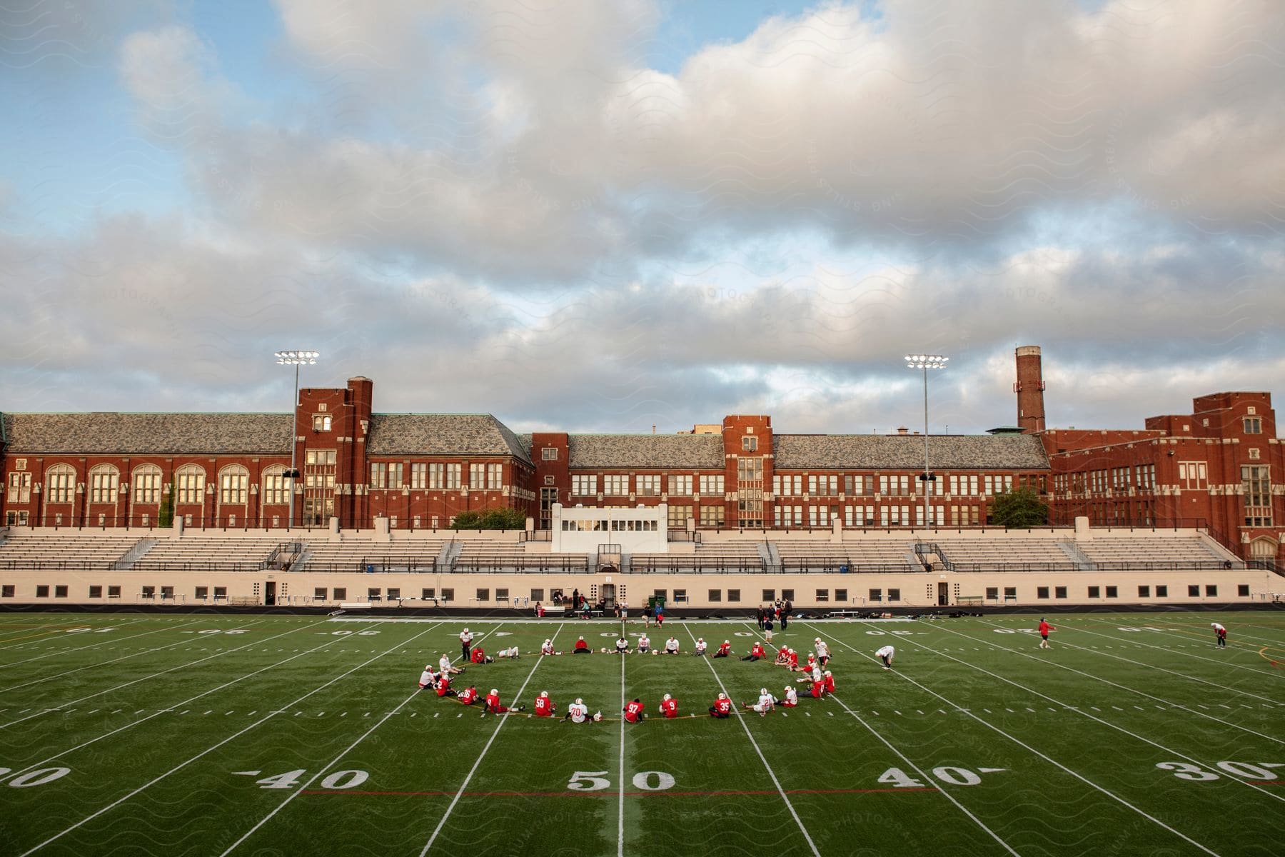 A team of athletes sitting in a circle in the middle of an American football field.