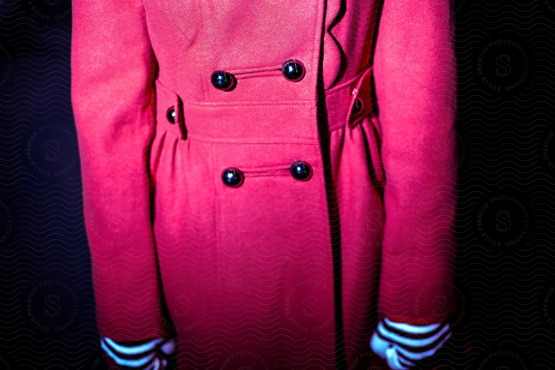 A pink coat with four black buttons and striped white and black gloves