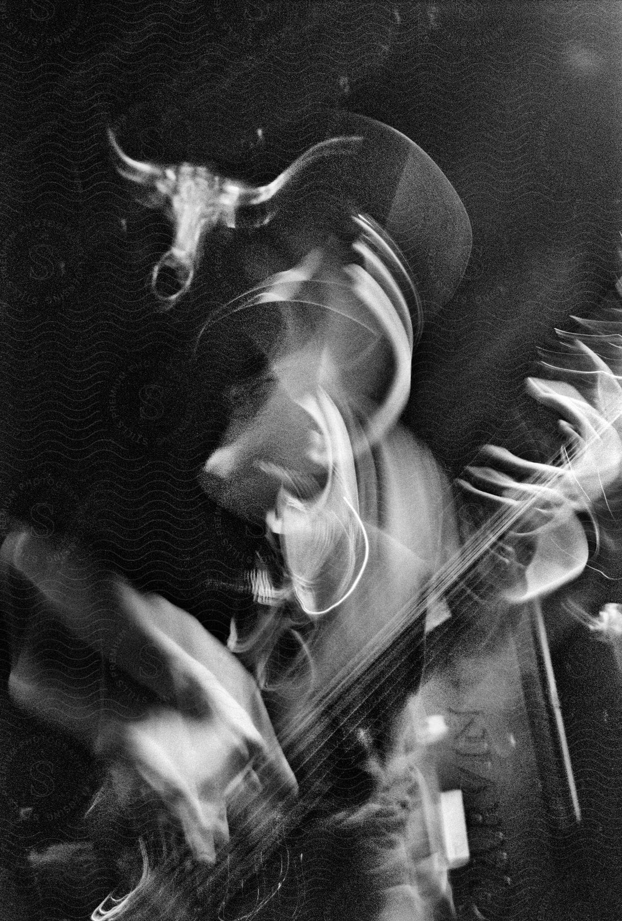A black and white photo captures a man's hands in motion blur as he plays a guitar creating trails of light.