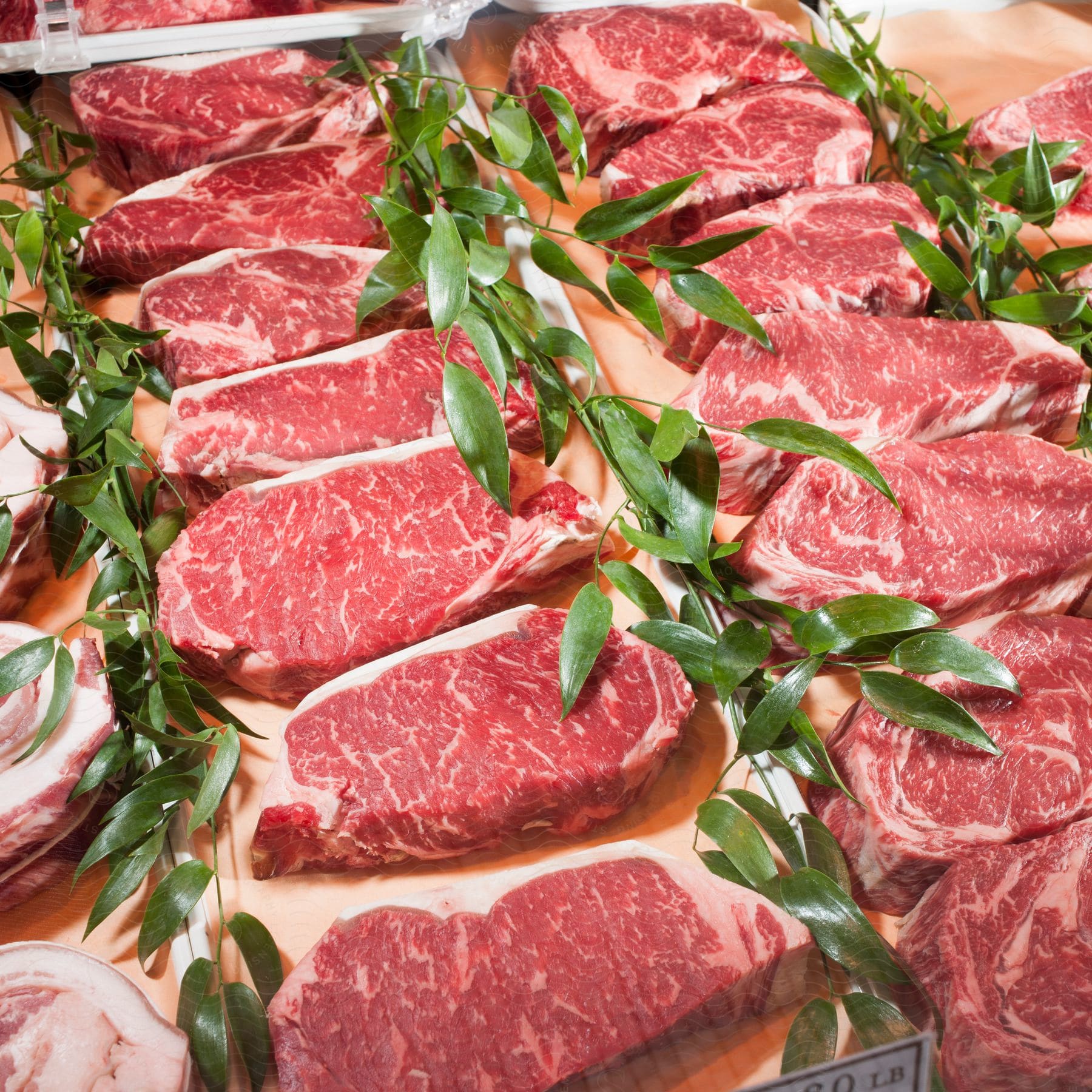 Several Pieces Of Raw Meat Arranged On A Platter With Sprigs Of Decorative Leaves