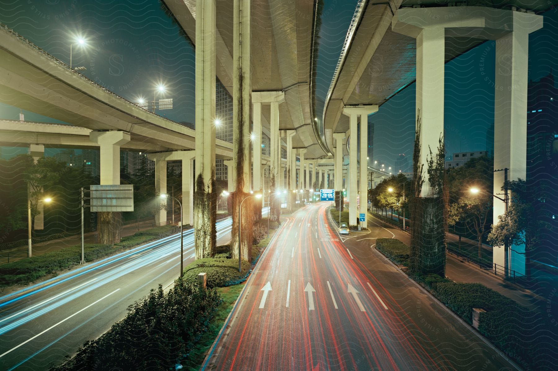 A multi lane highway is under another tall supported highway in a city at night with no cars driving.