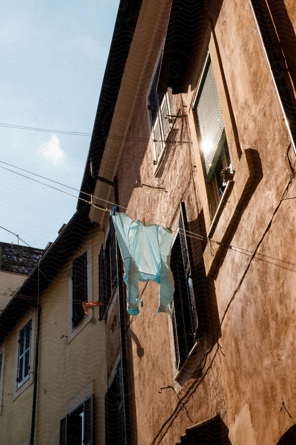 A shirt drying on a rope outside the windows of a rural brown building on a sunny day.