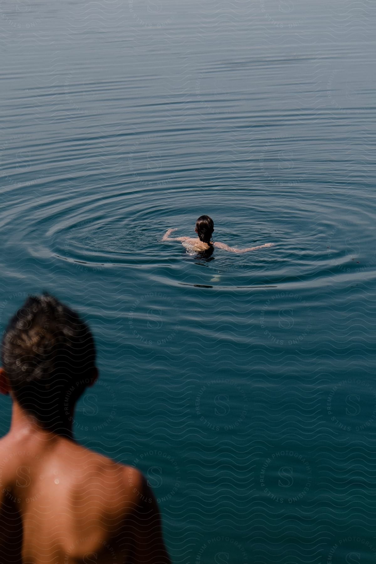 Ripples spread outward from where a woman is swimming in a lake as her male companion watches nearby.