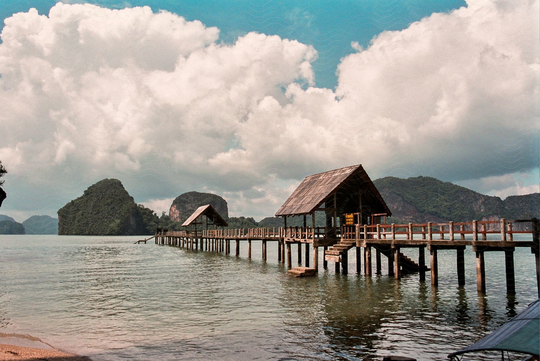 A pier with huts made of wood on a sea shore with green hills in the background.