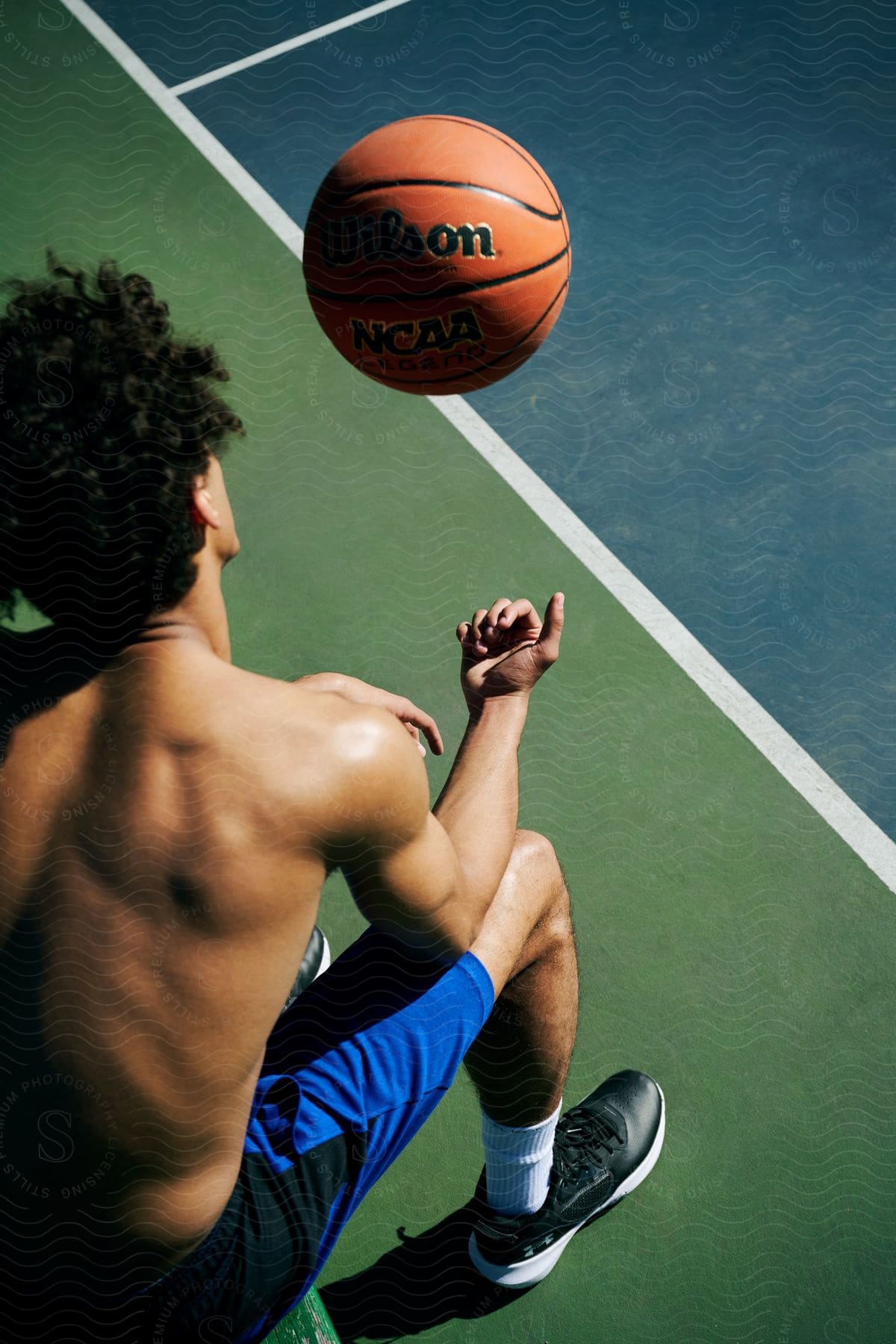 A seated boy is throwing an orange basketball in the air across a court.