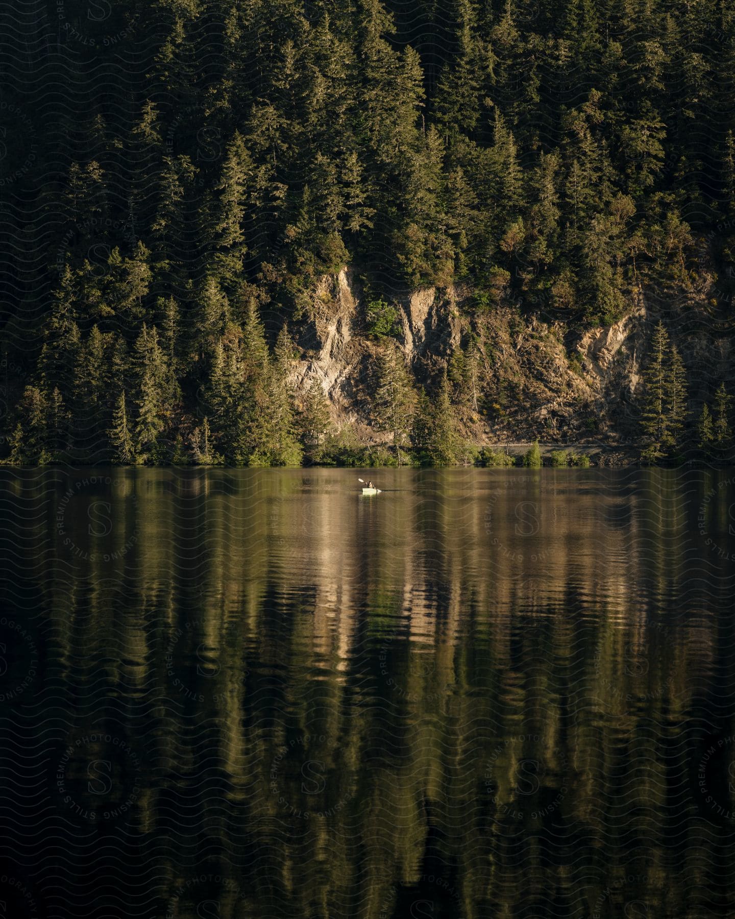 A person in a canoe paddling on a lake towards a forest cliff face.