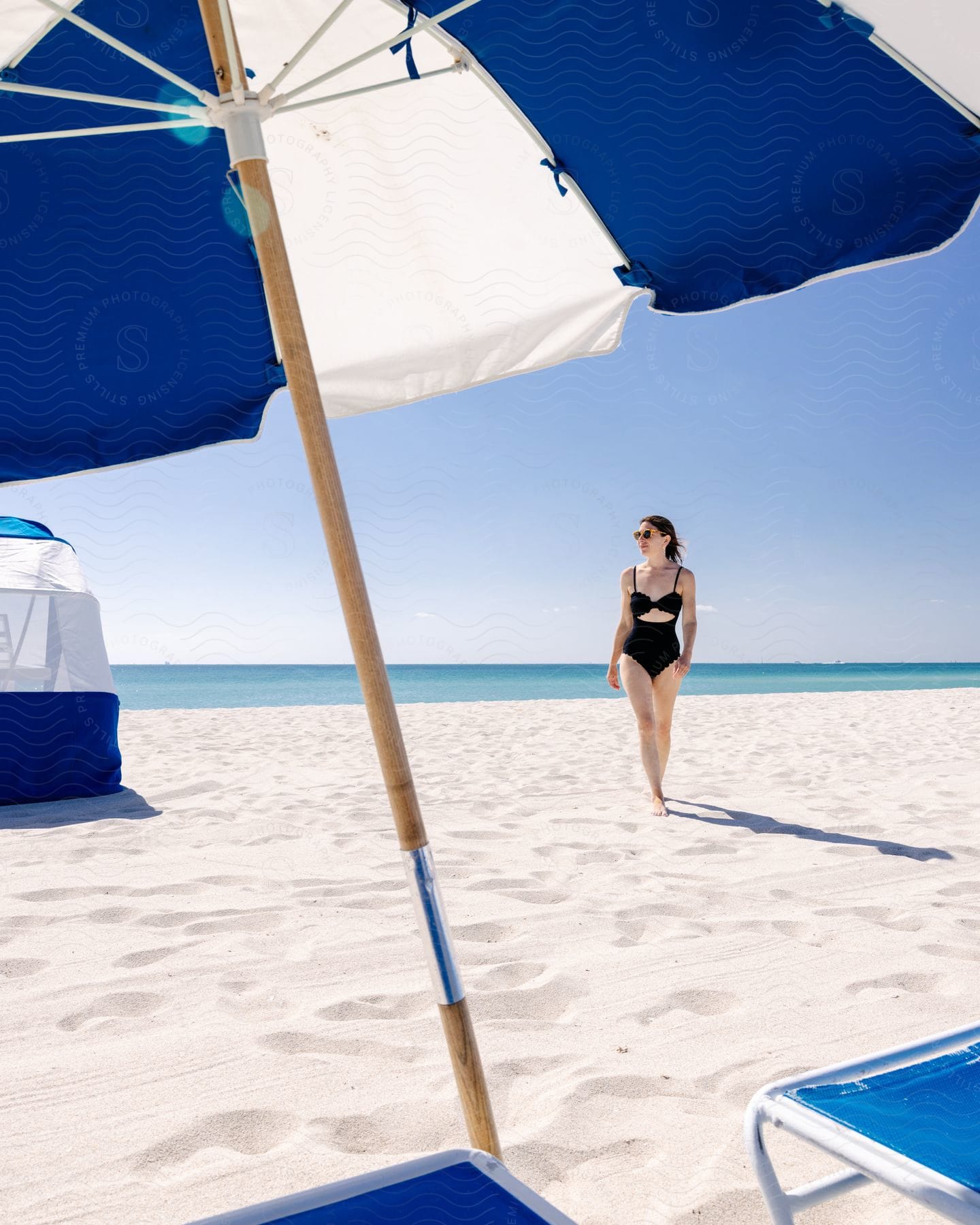 a woman walks along the beach toward an umbrella and lawn chairs