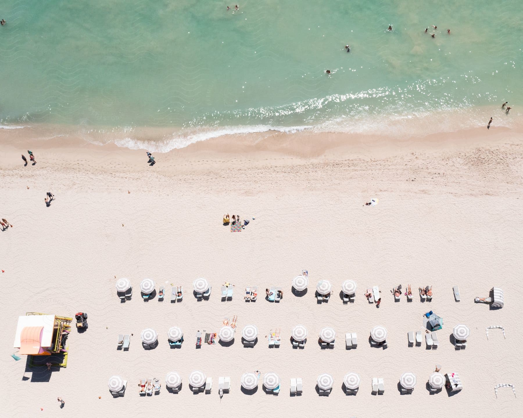 Several umbrellas and chairs on the sand of a beach with several people and very clear water.