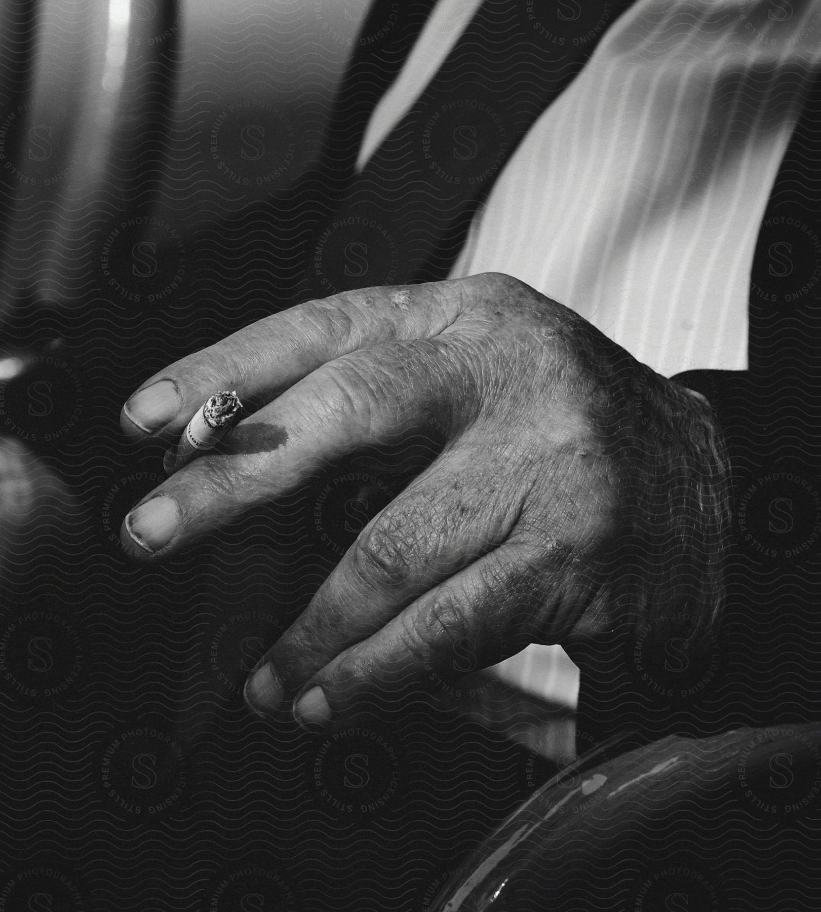 A cigarette resting in a man's hands while he is sitting