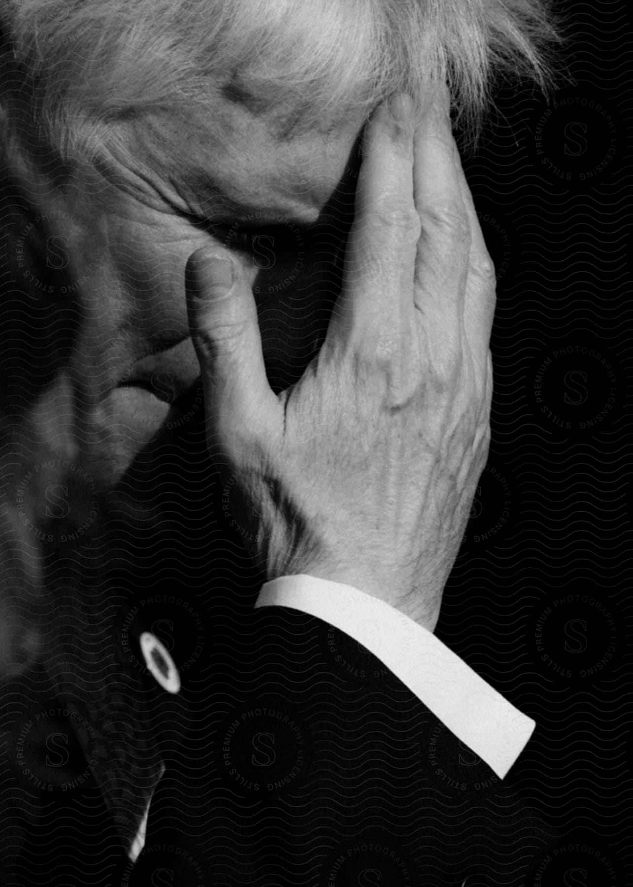 Man in a suit with his hand resting on his forehead and face.