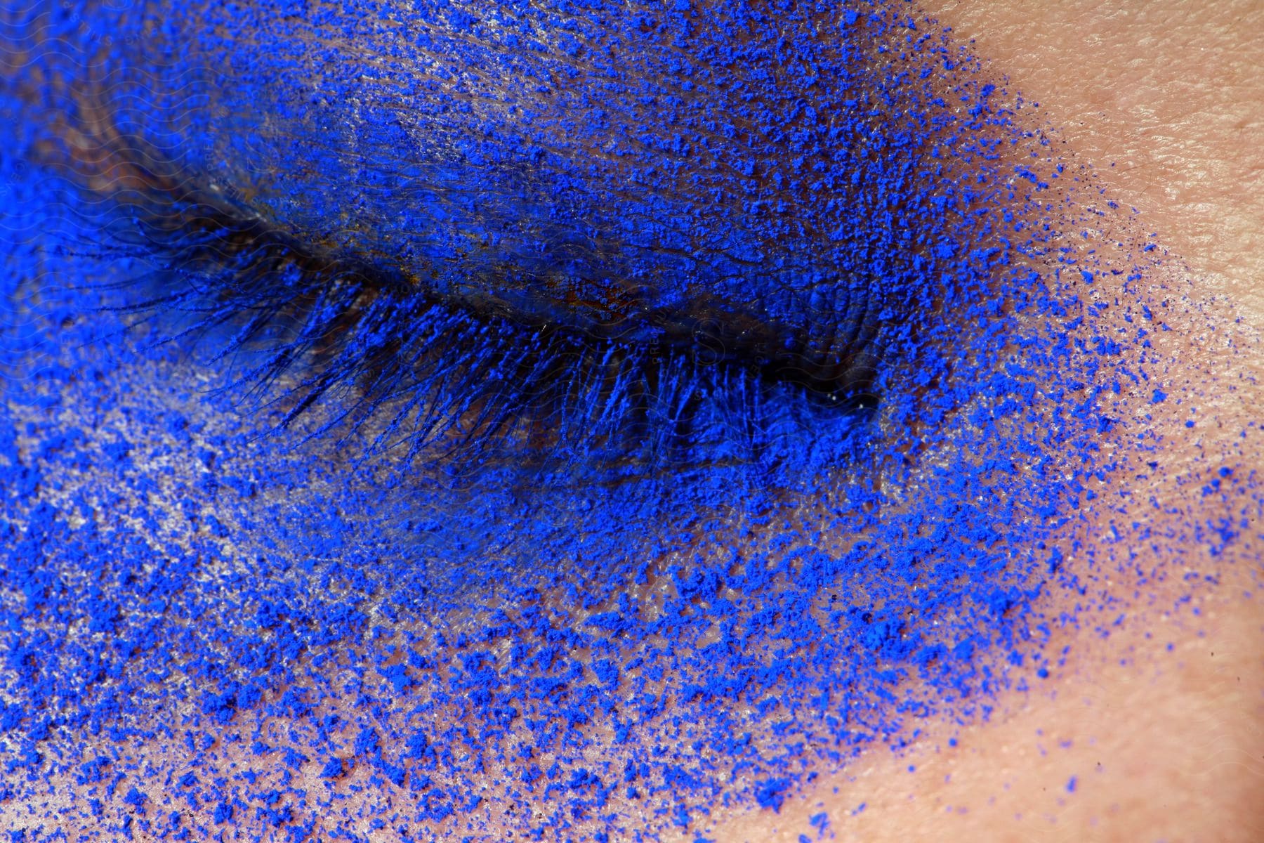 Blue eye shadow powder dusted over the closed eye of a woman.