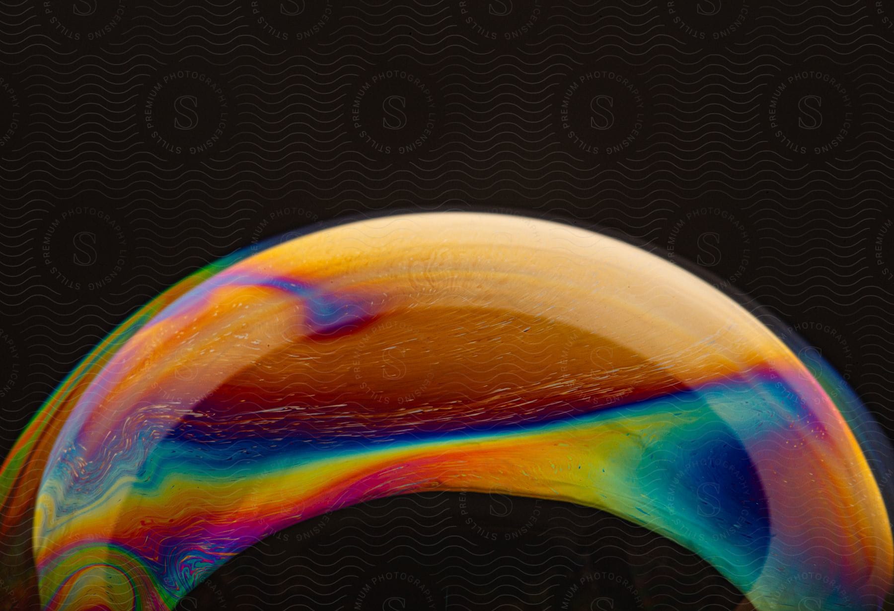 A close-up view of a soap bubble's colorful surface, illuminated against a dark background