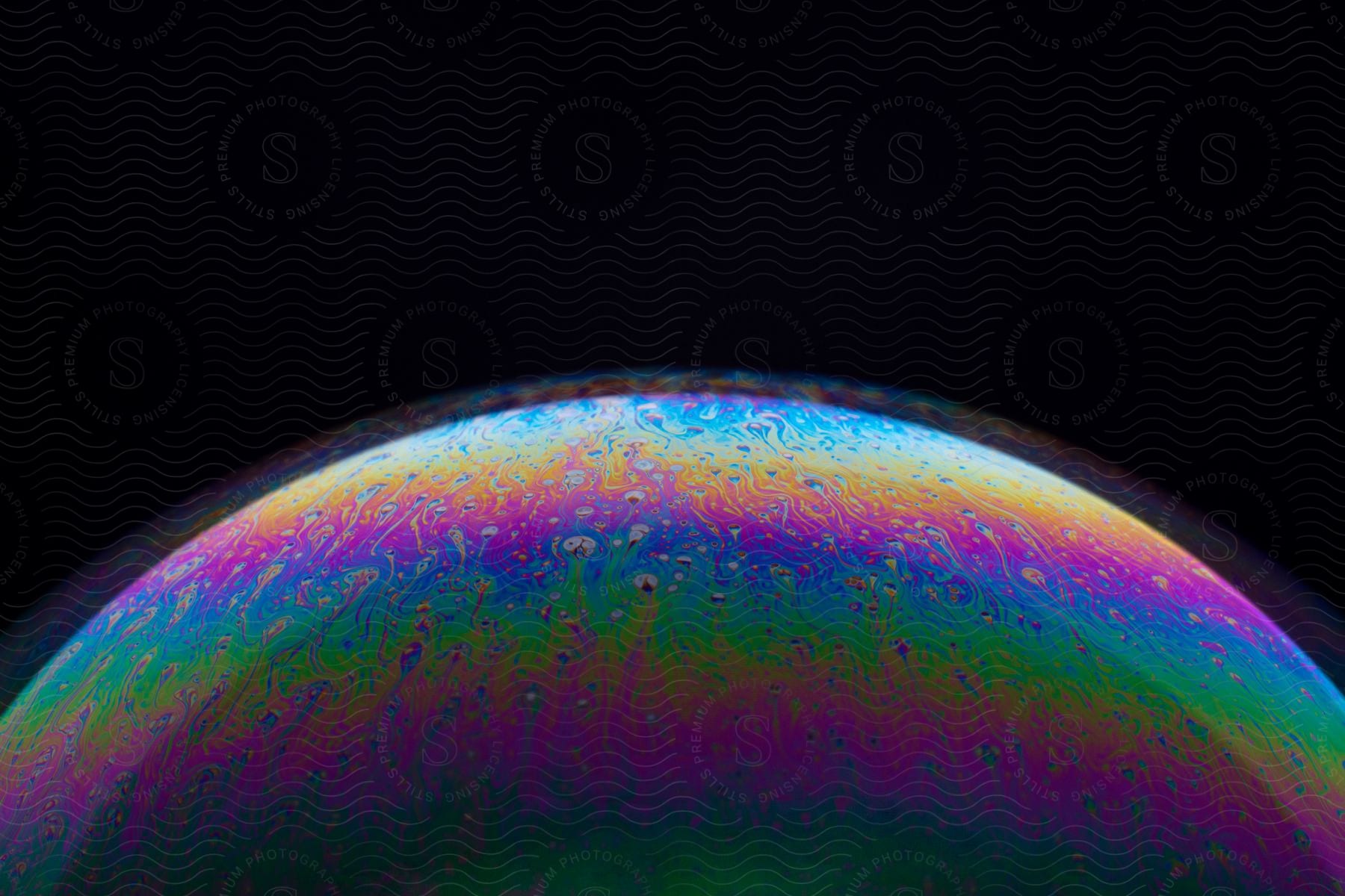 A close-up view of a soap bubble's colorful rainbow surface, illuminated against a dark background