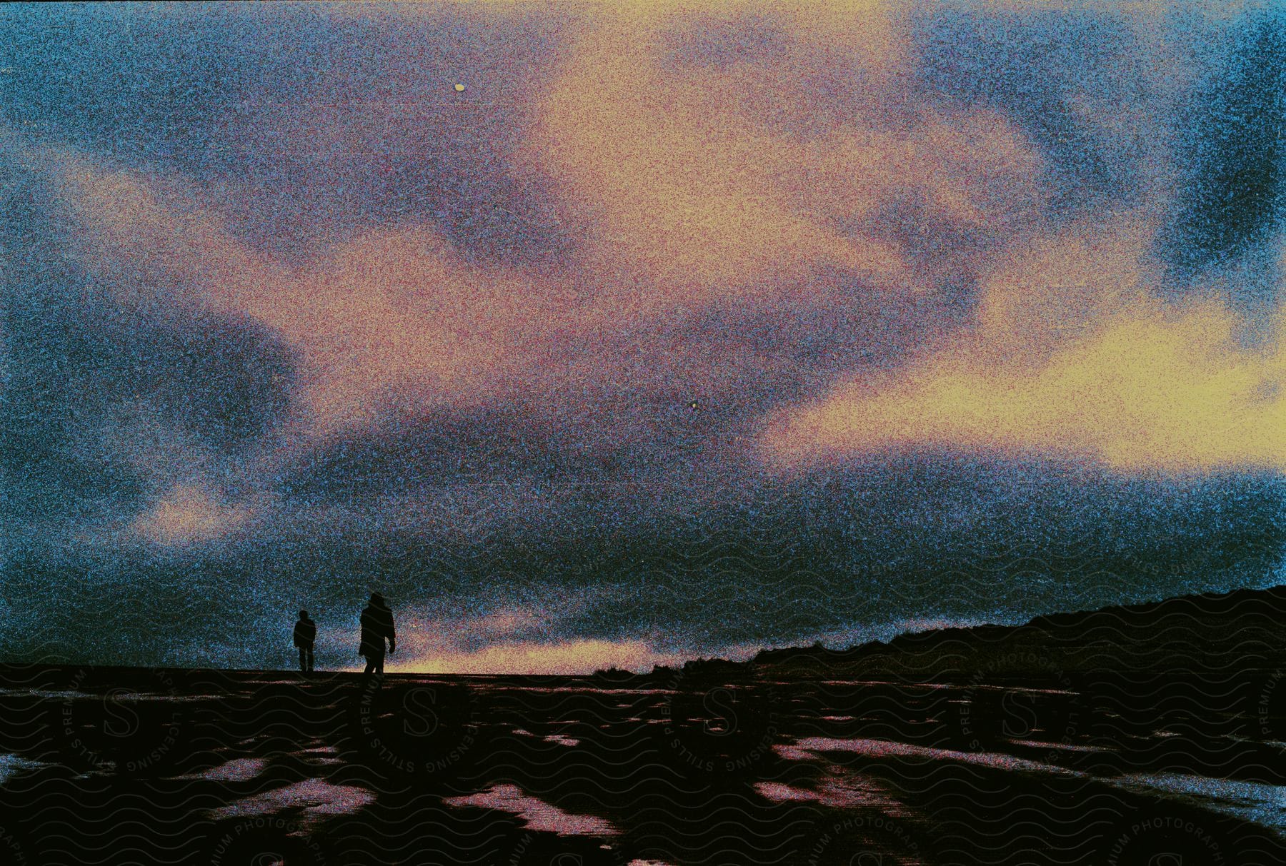 Two people stand on a grassy plain under a cloudy night sky with patches of snow on the ground.